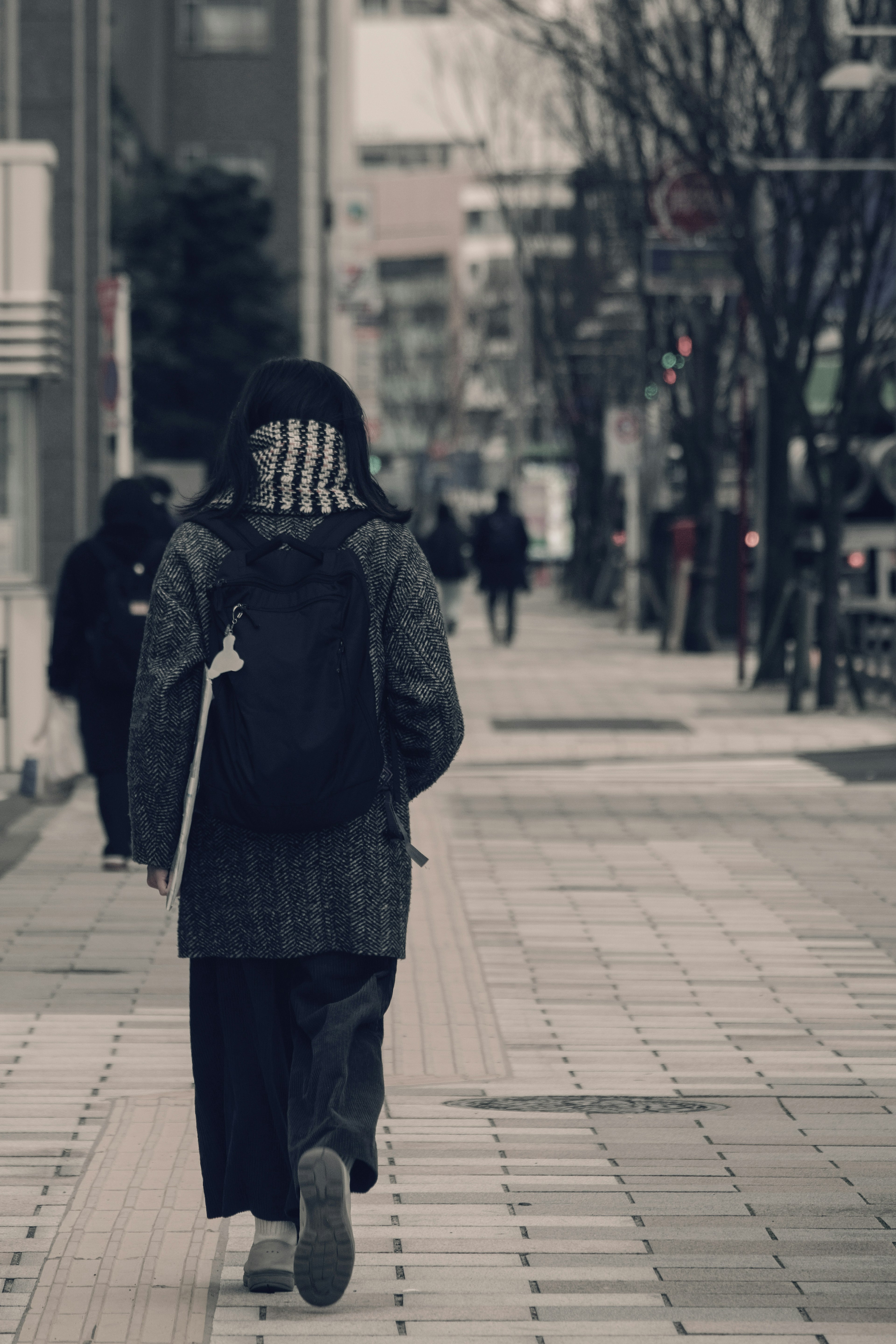 A person walking in the city wearing dark clothing with a backpack surrounded by other pedestrians