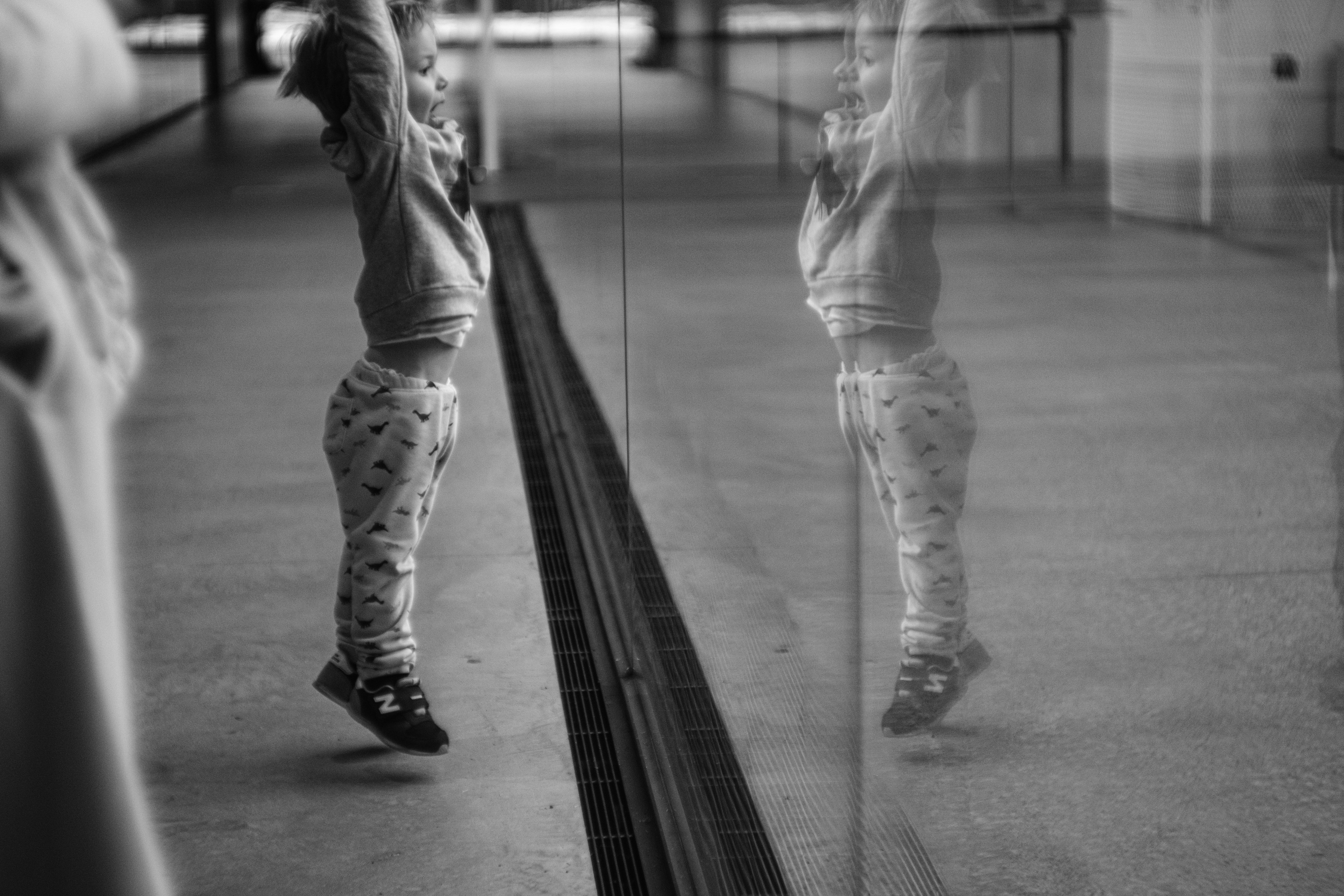 Black and white photo of a child jumping in front of glass