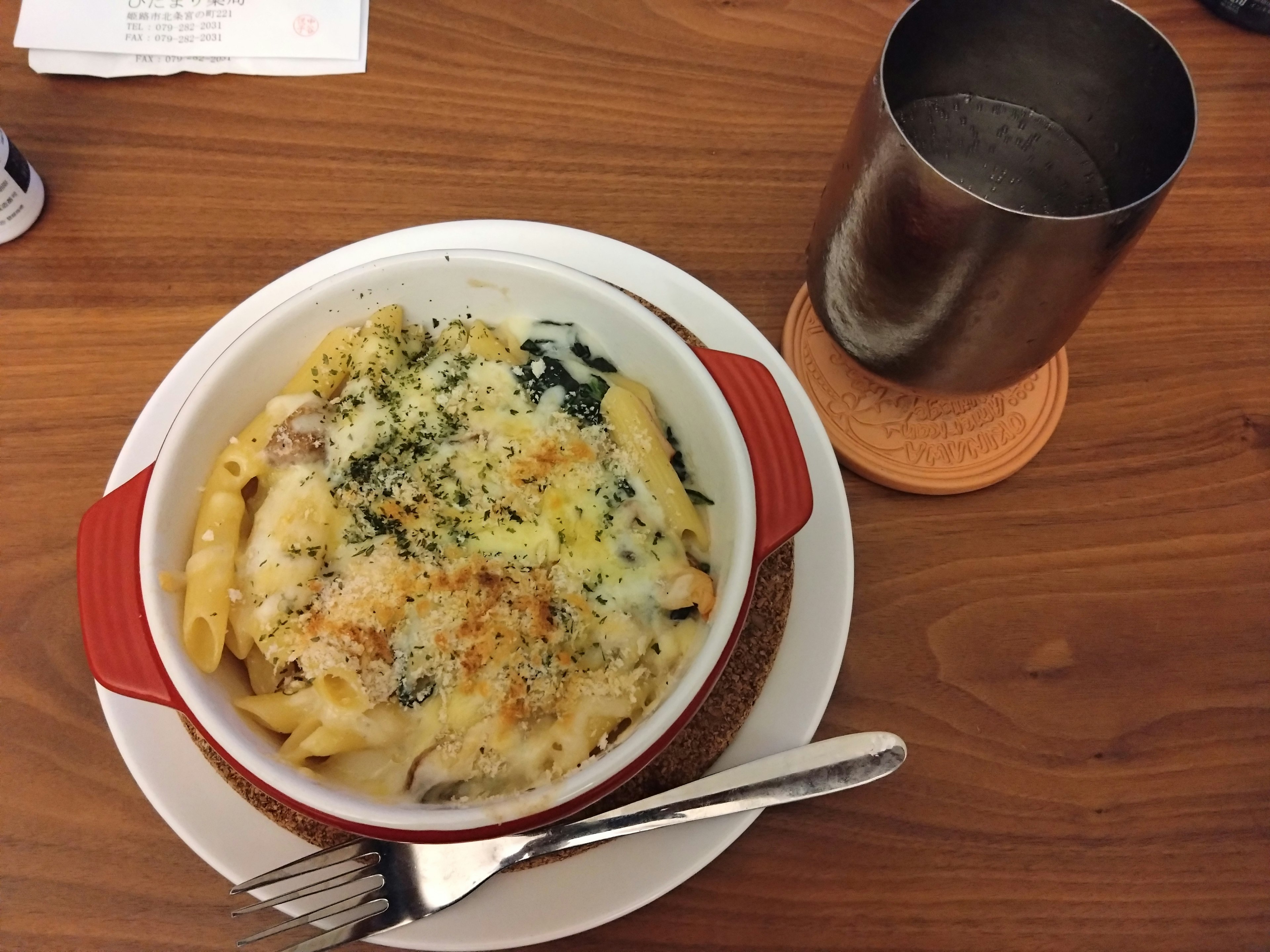 Gratin de macaroni au four dans un plat rouge avec une tasse en métal à côté