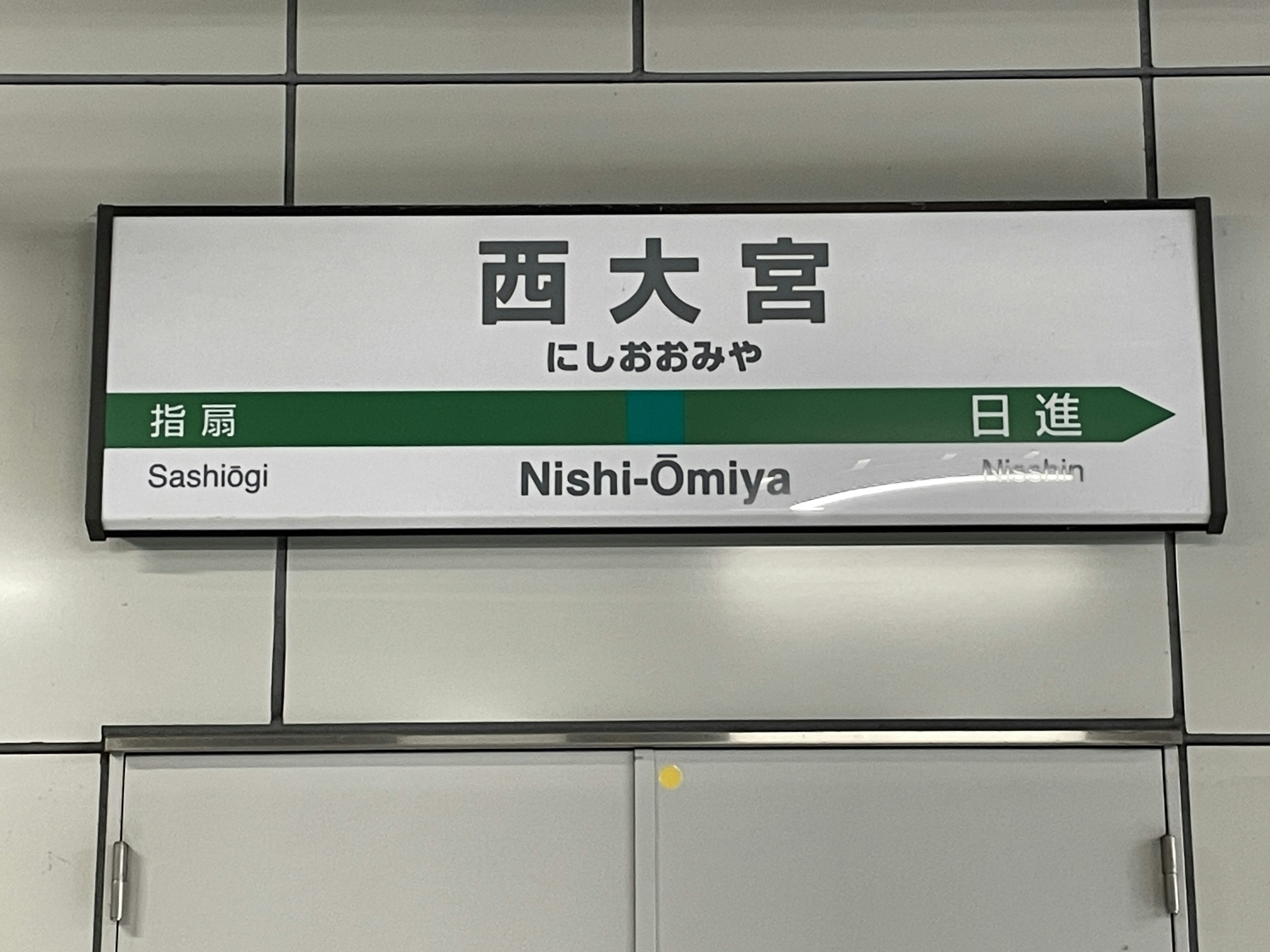 Sign for Nishi-Omiya Station with directional green arrow