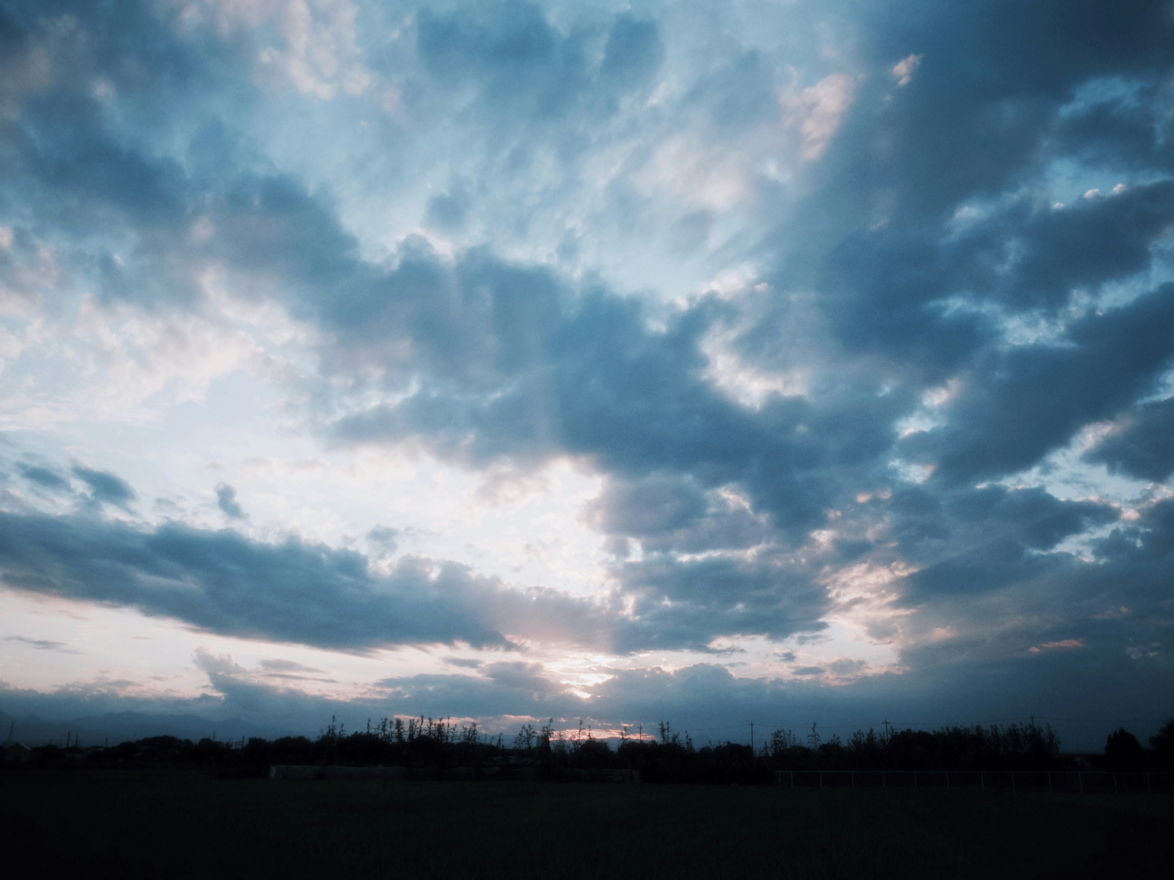 Un paisaje con un cielo azul lleno de nubes y un atardecer visible