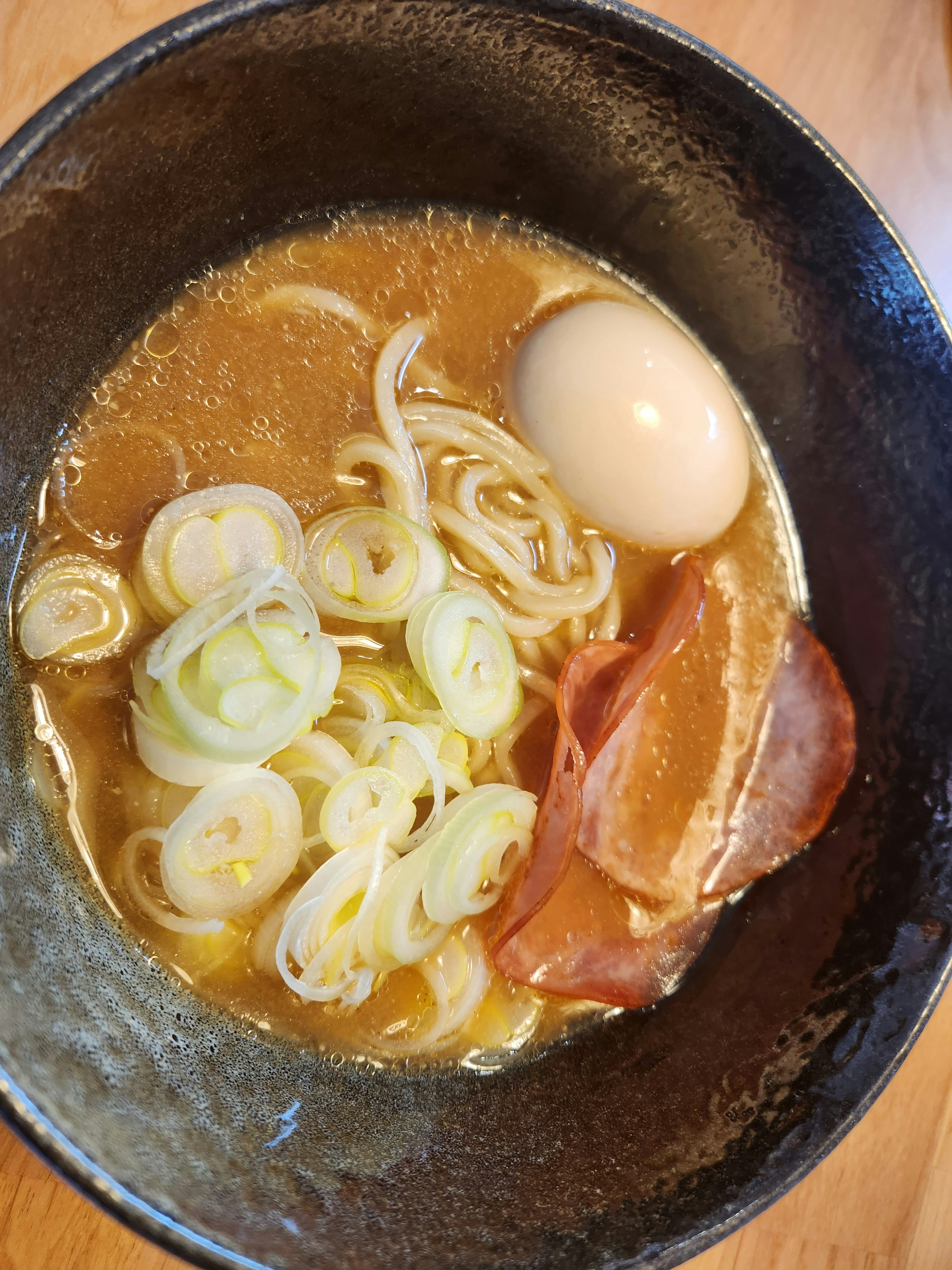 Bowl of ramen with broth, sliced green onions, soft-boiled egg, and chashu pork