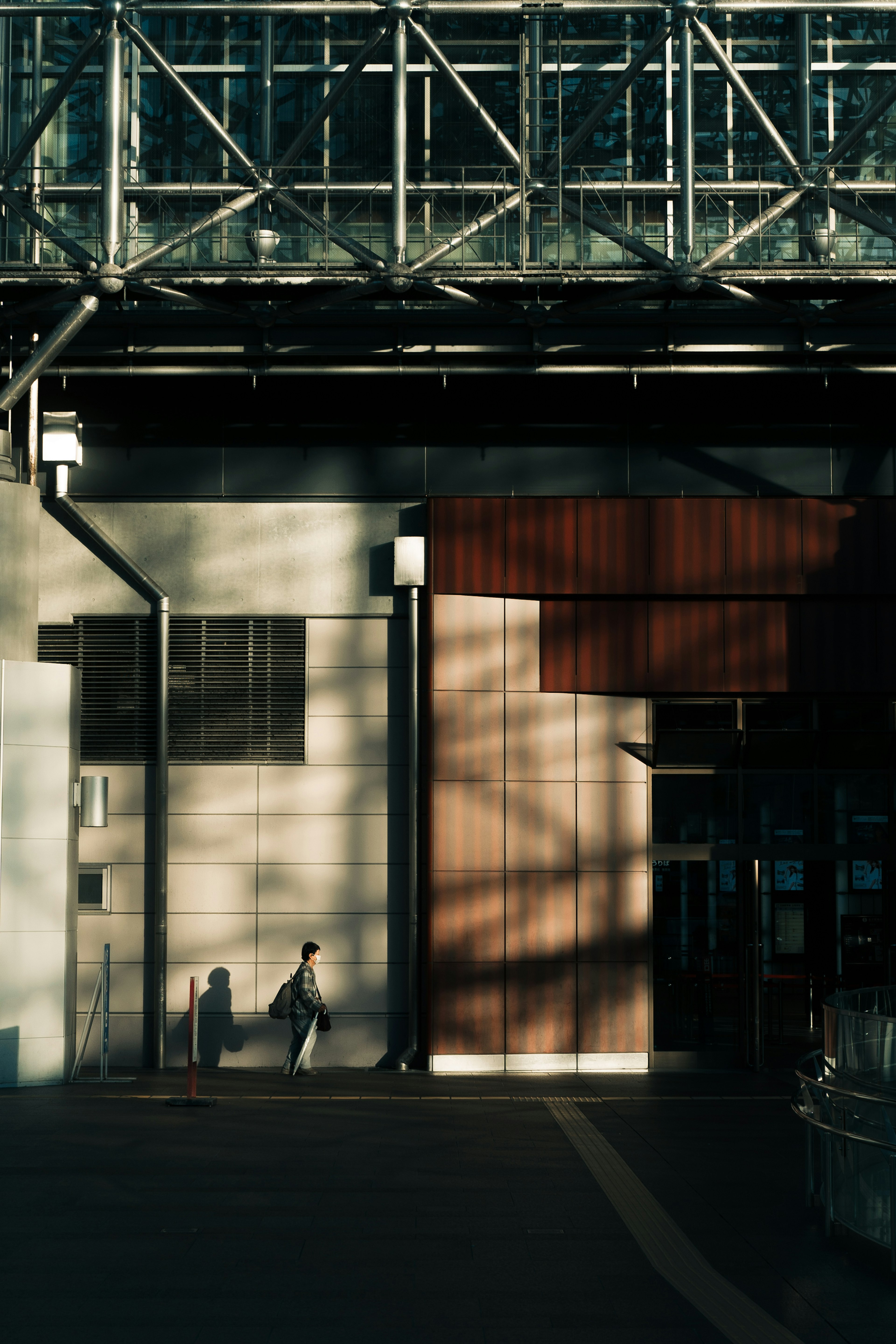 A person walking in front of a modern building featuring shadows and structural elements