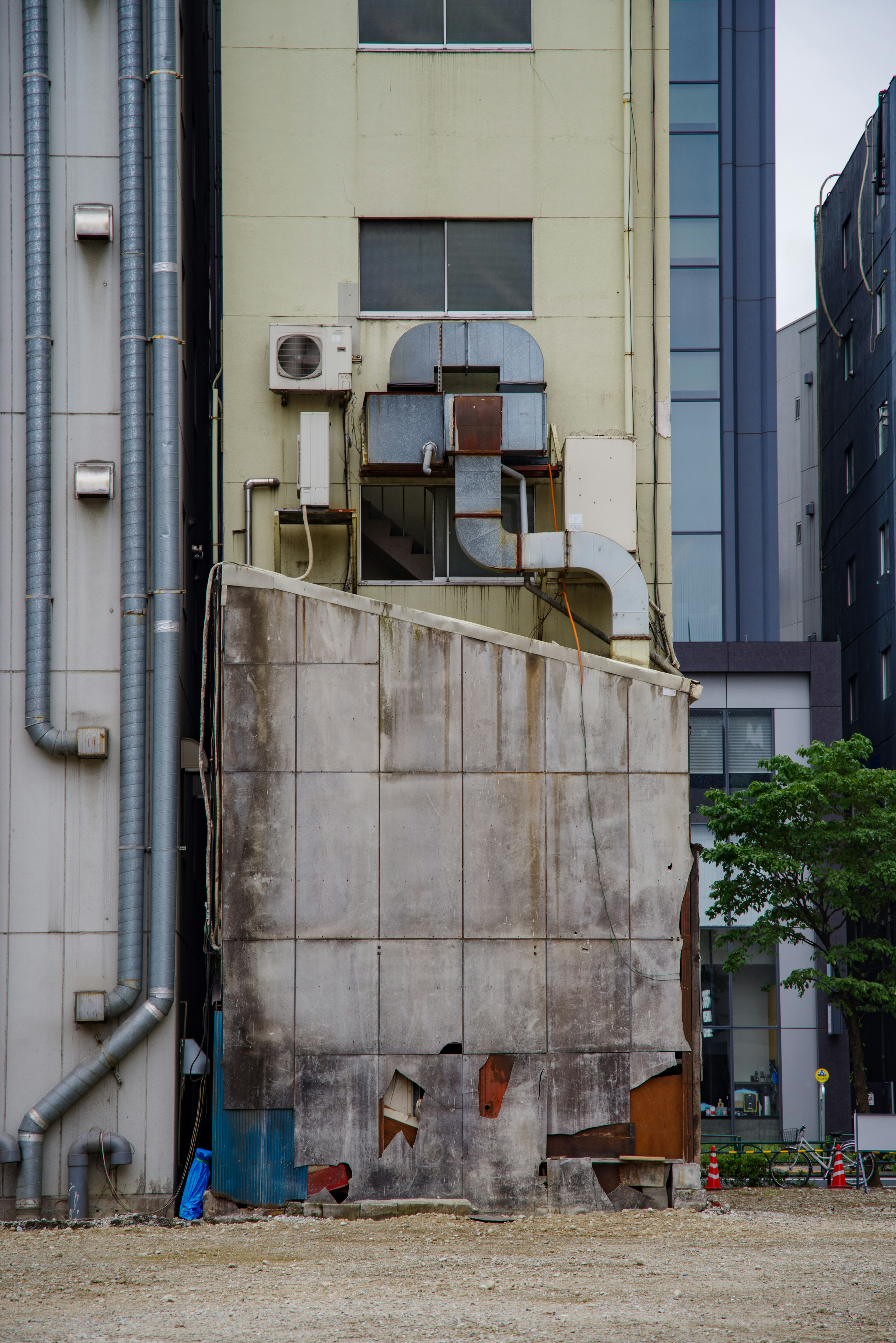 Partial wall of a building showing exposed air conditioning units and piping