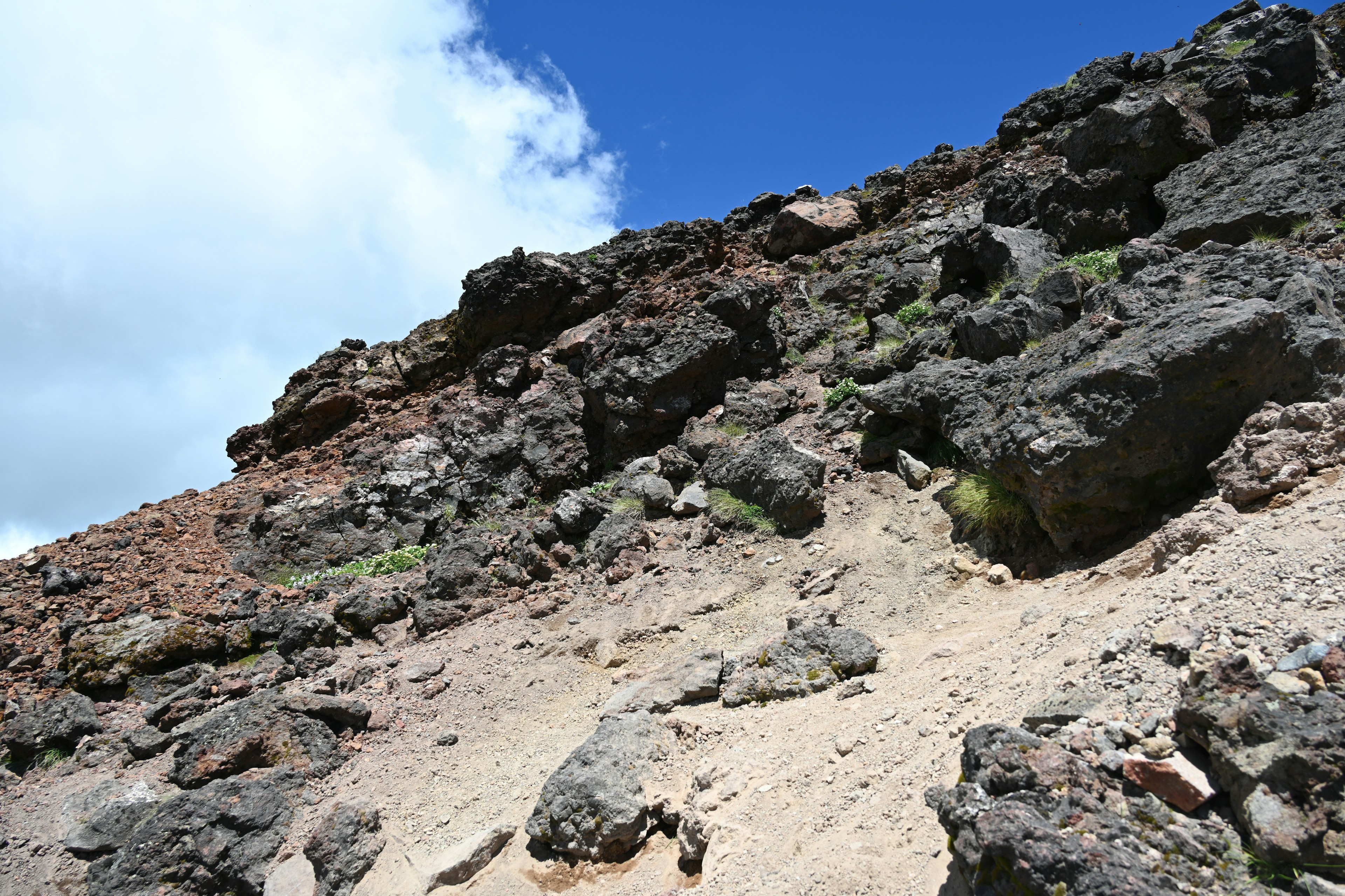 Eine felsige Steigung mit Sand und Vegetationsflecken unter einem blauen Himmel