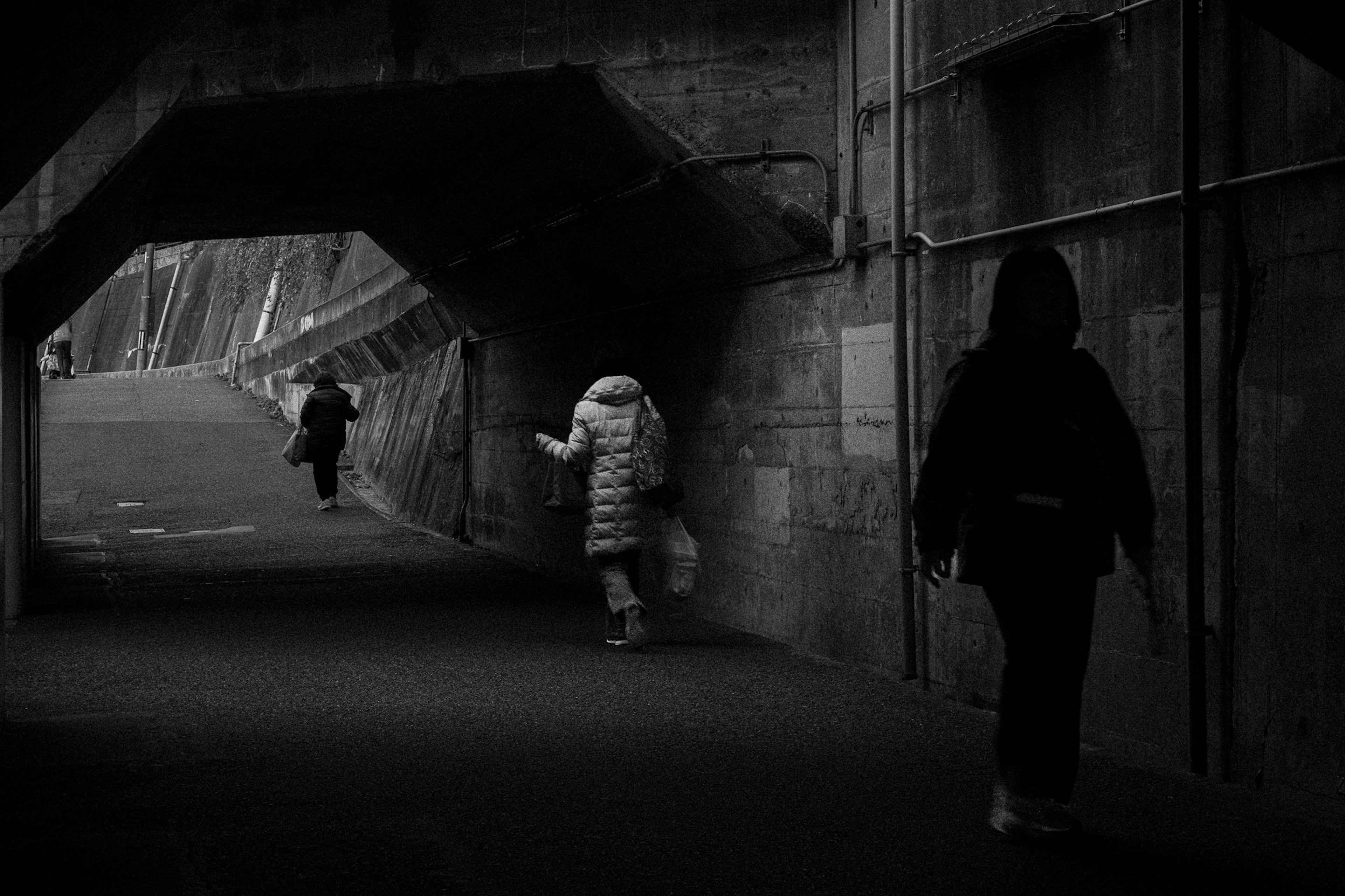 People walking through a dark tunnel with contrasting shadows