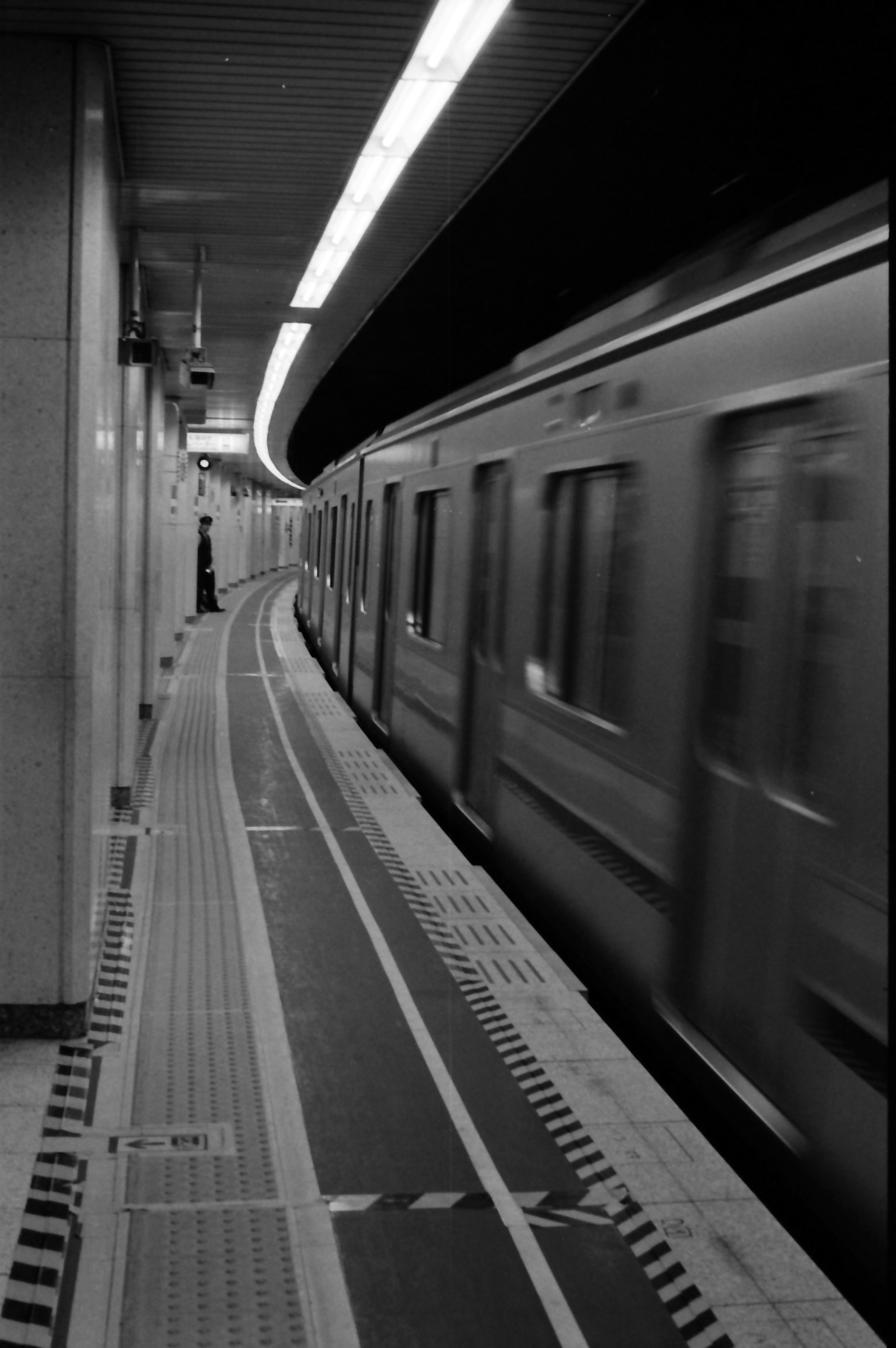 Estación de metro en blanco y negro con plataforma curva y tren que pasa