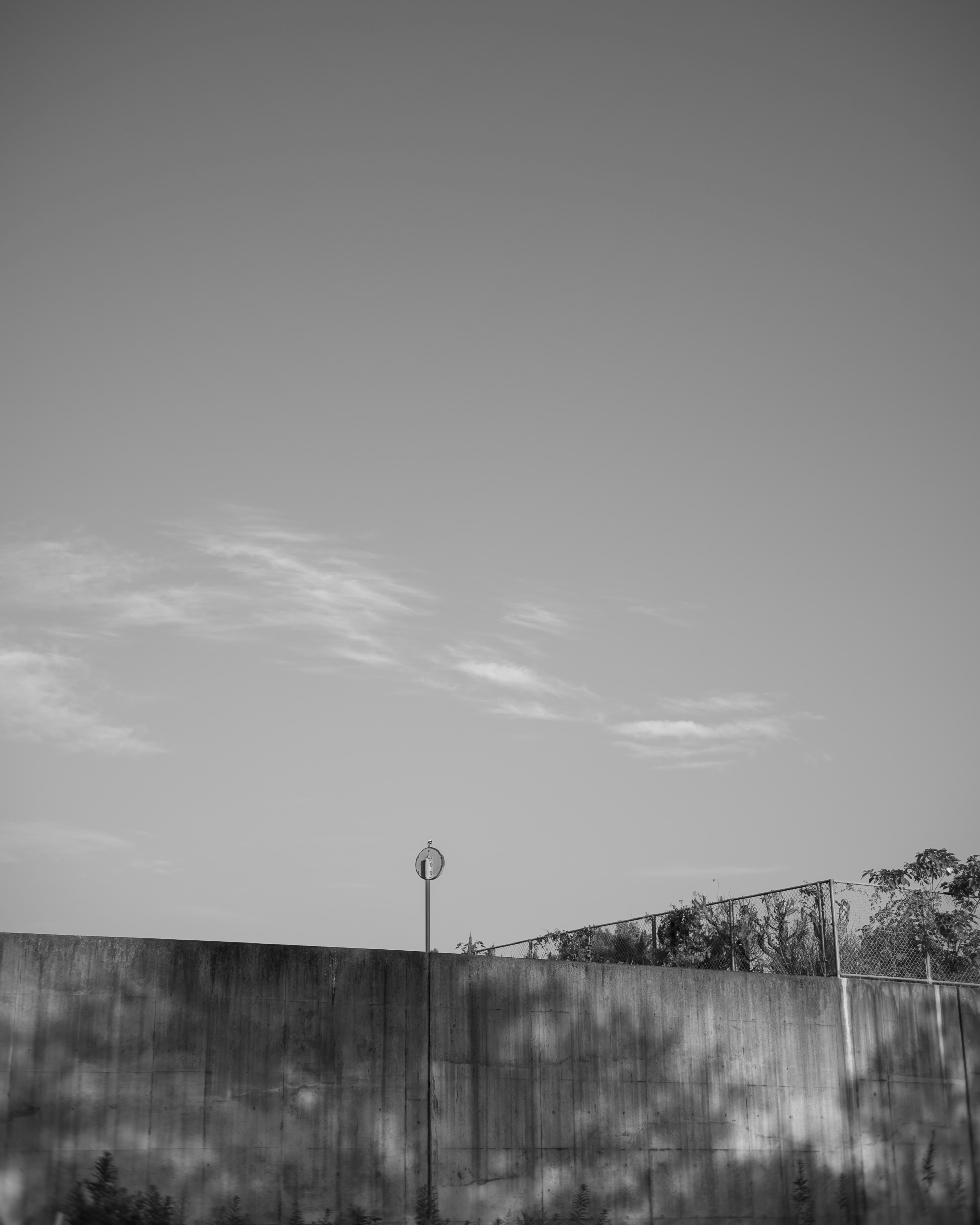 Black and white landscape photo featuring clouds in the sky with a tall wall and a pole in the foreground