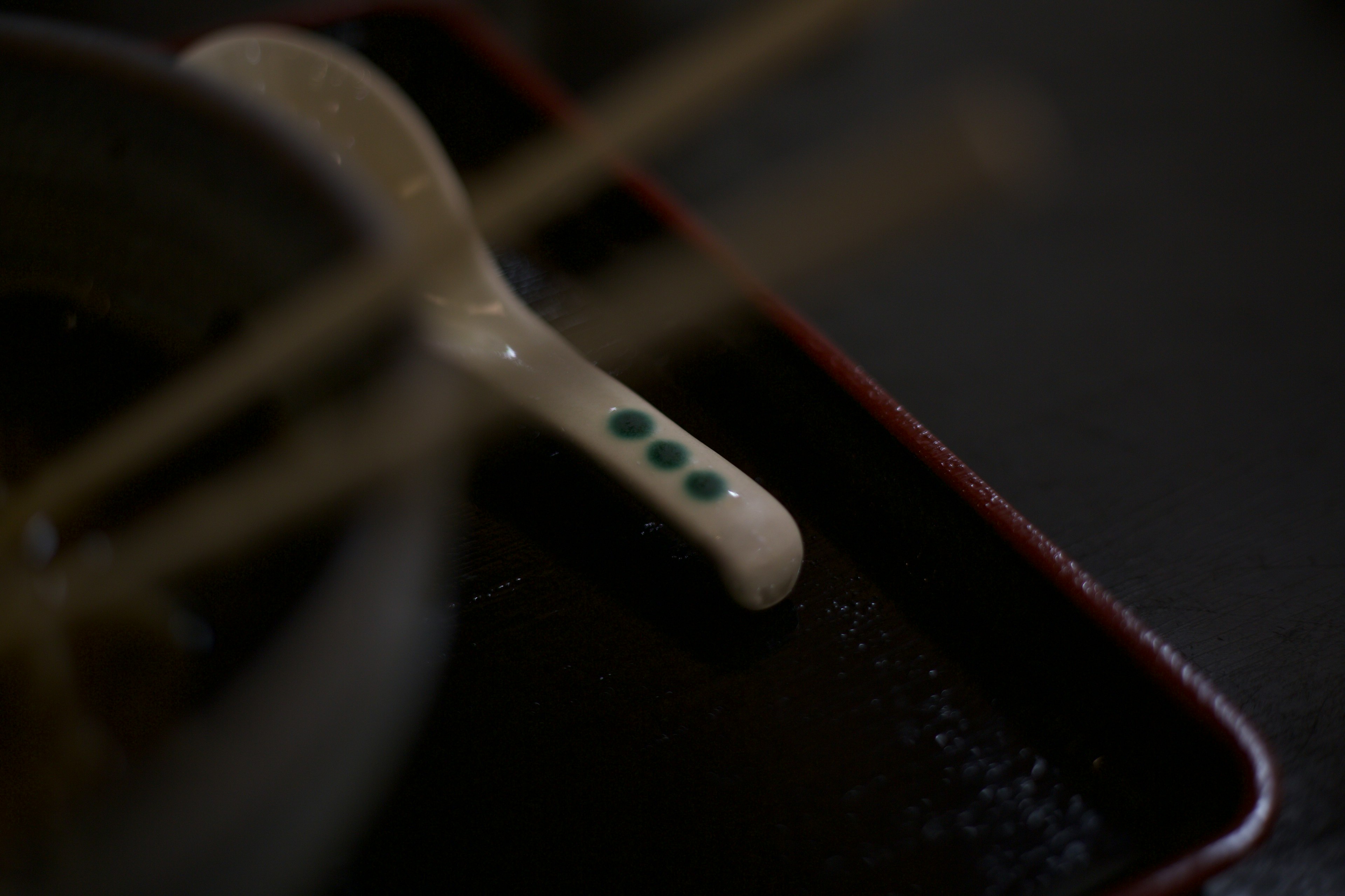 Close-up of a white spoon with green dots and chopsticks on a black plate