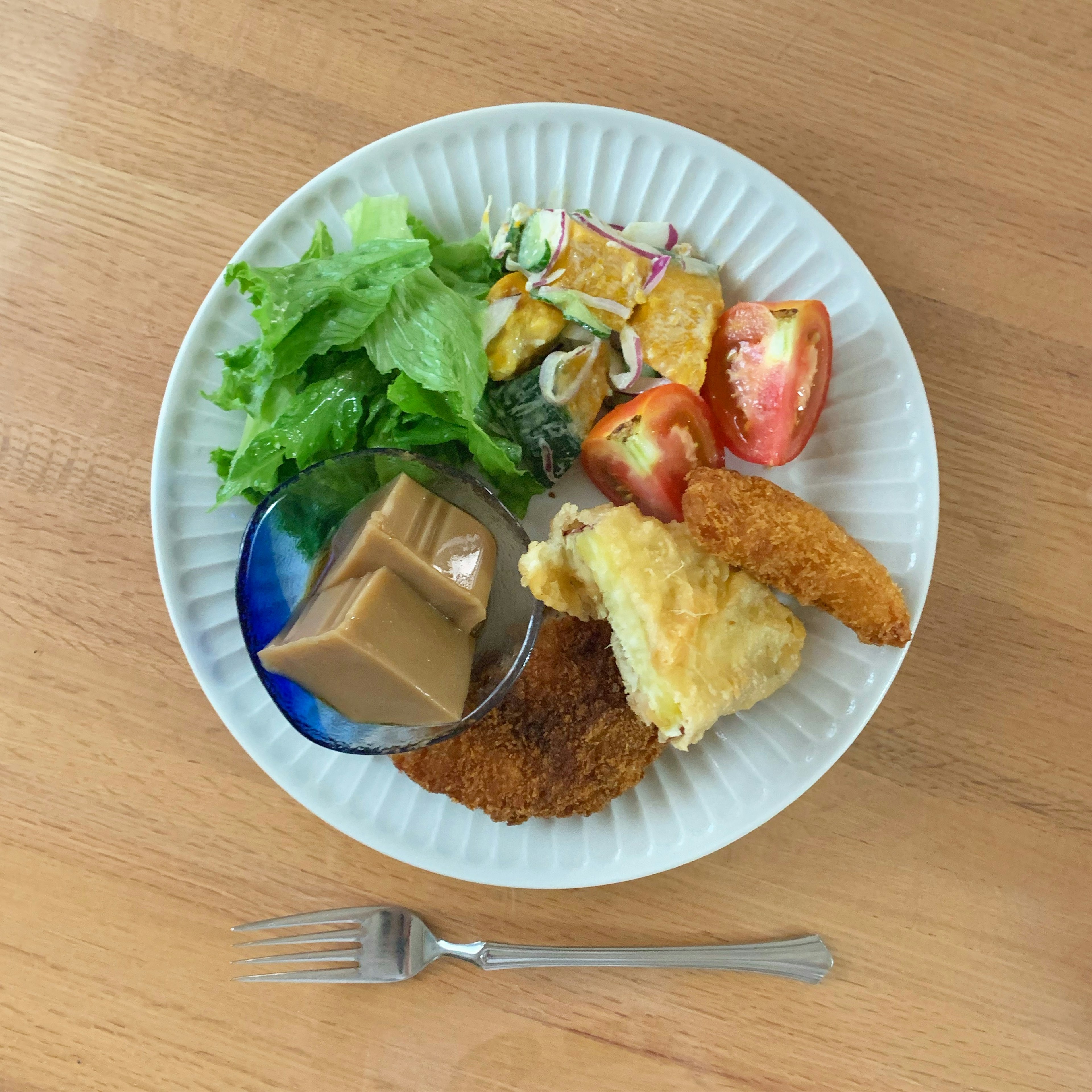 Un plato con ensalada, tomate, alimentos fritos y un pudín de postre