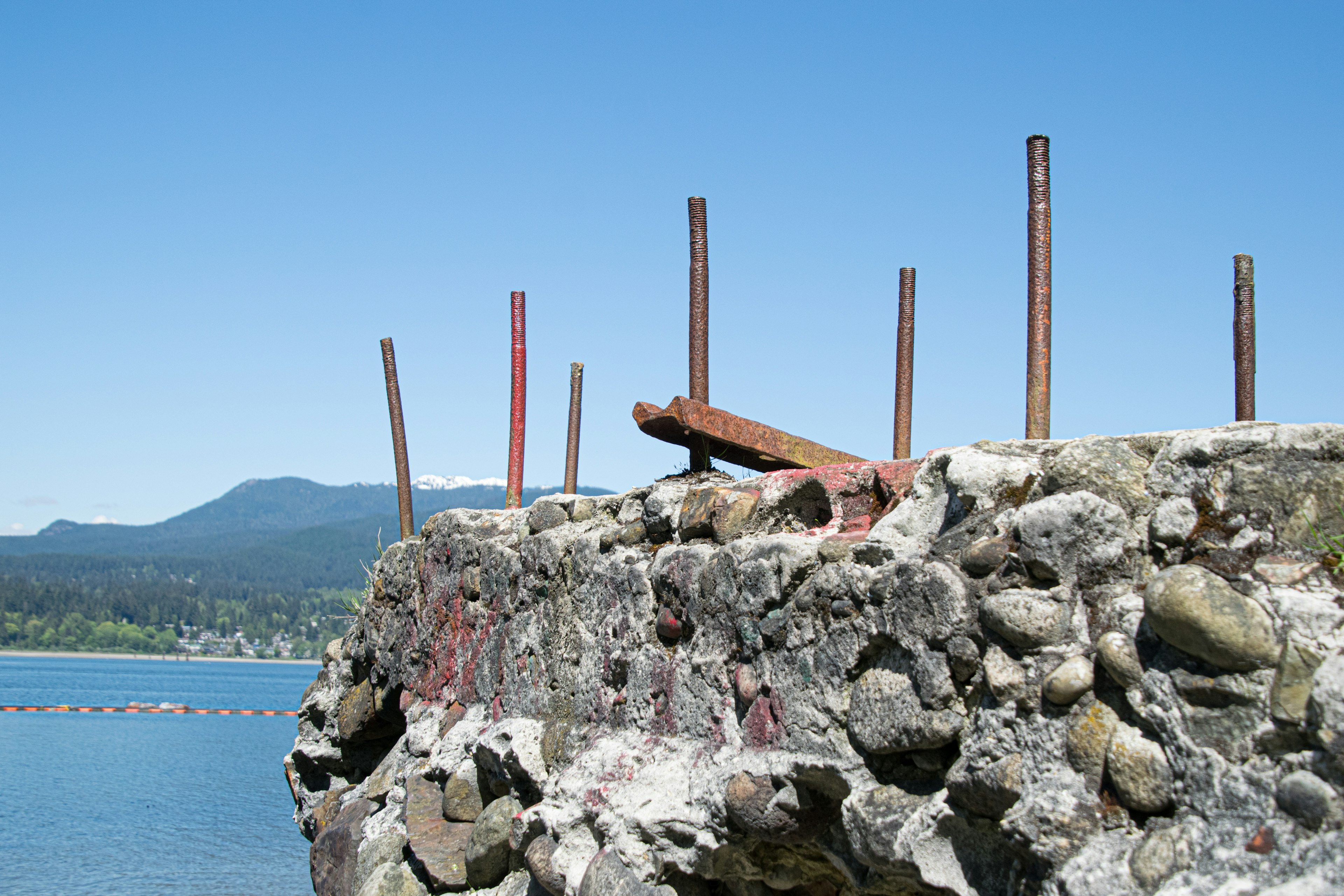 A rocky shoreline with protruding metal poles against a blue sky