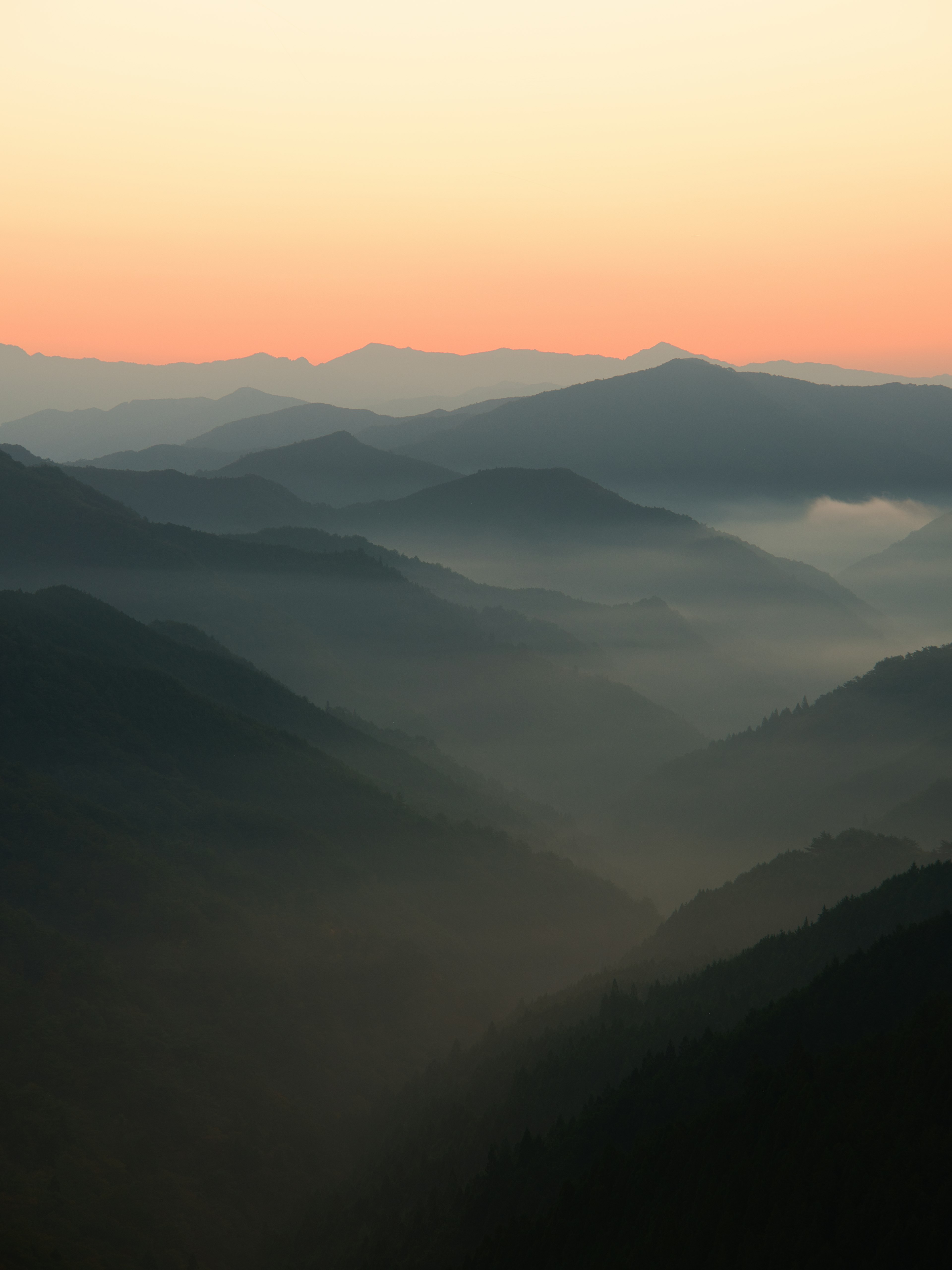 Gunung berkabut dengan langit oranye lembut saat fajar