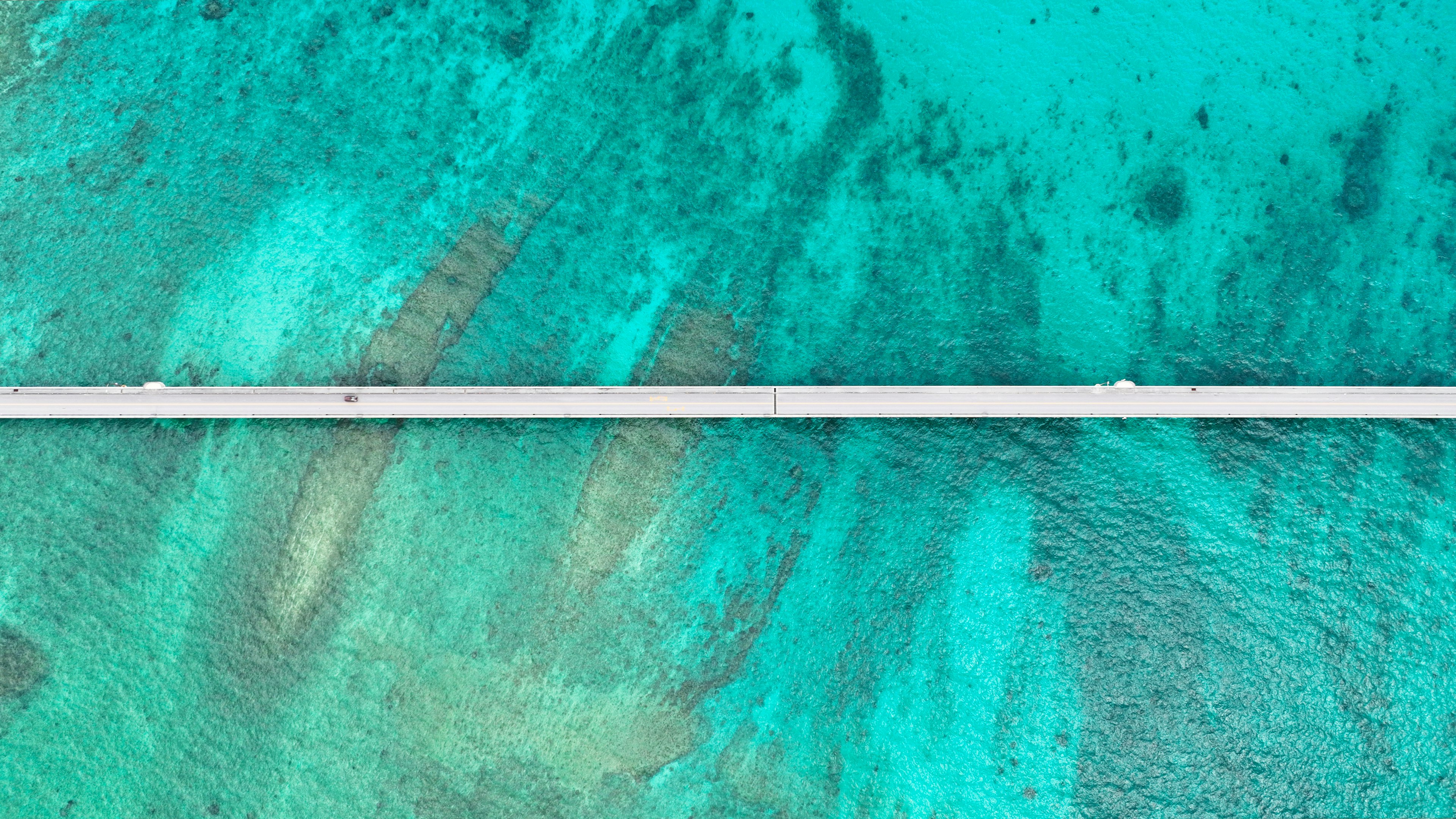 Aerial view of turquoise water with a white pier