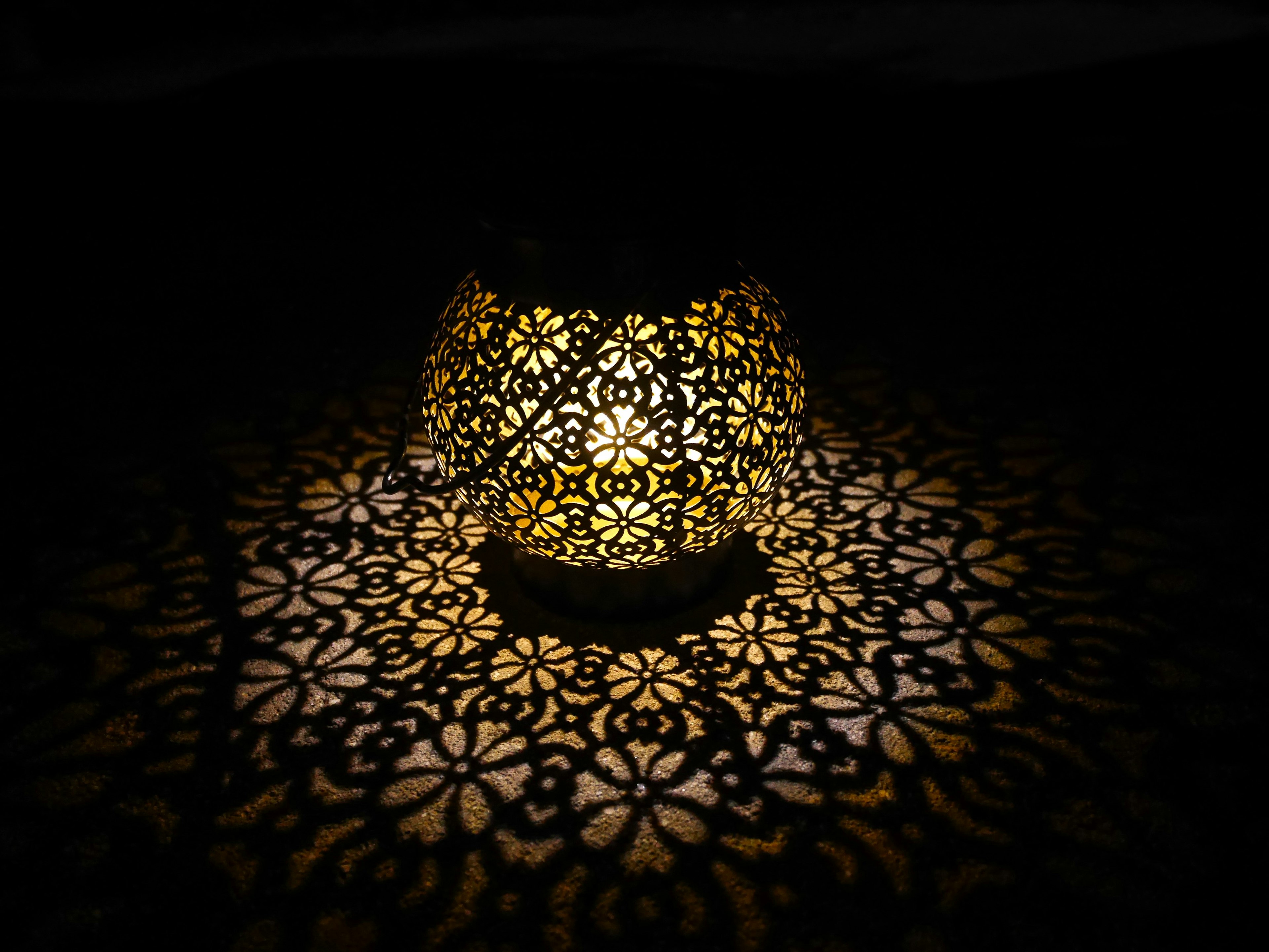 Decorative lamp emitting light with floral patterns cast in shadow