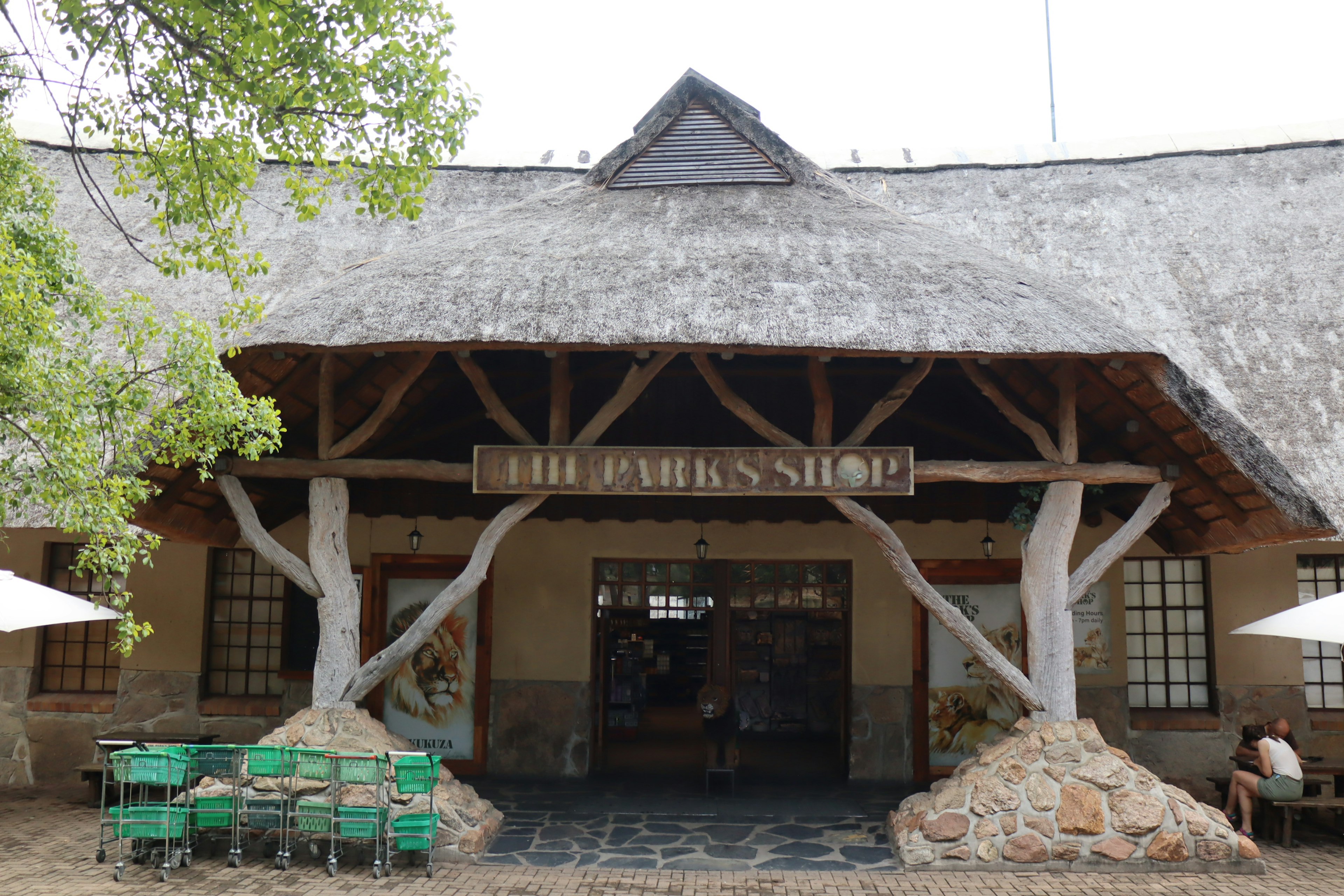 Exterior of a park shop with a traditional thatched roof green chairs and tables in view