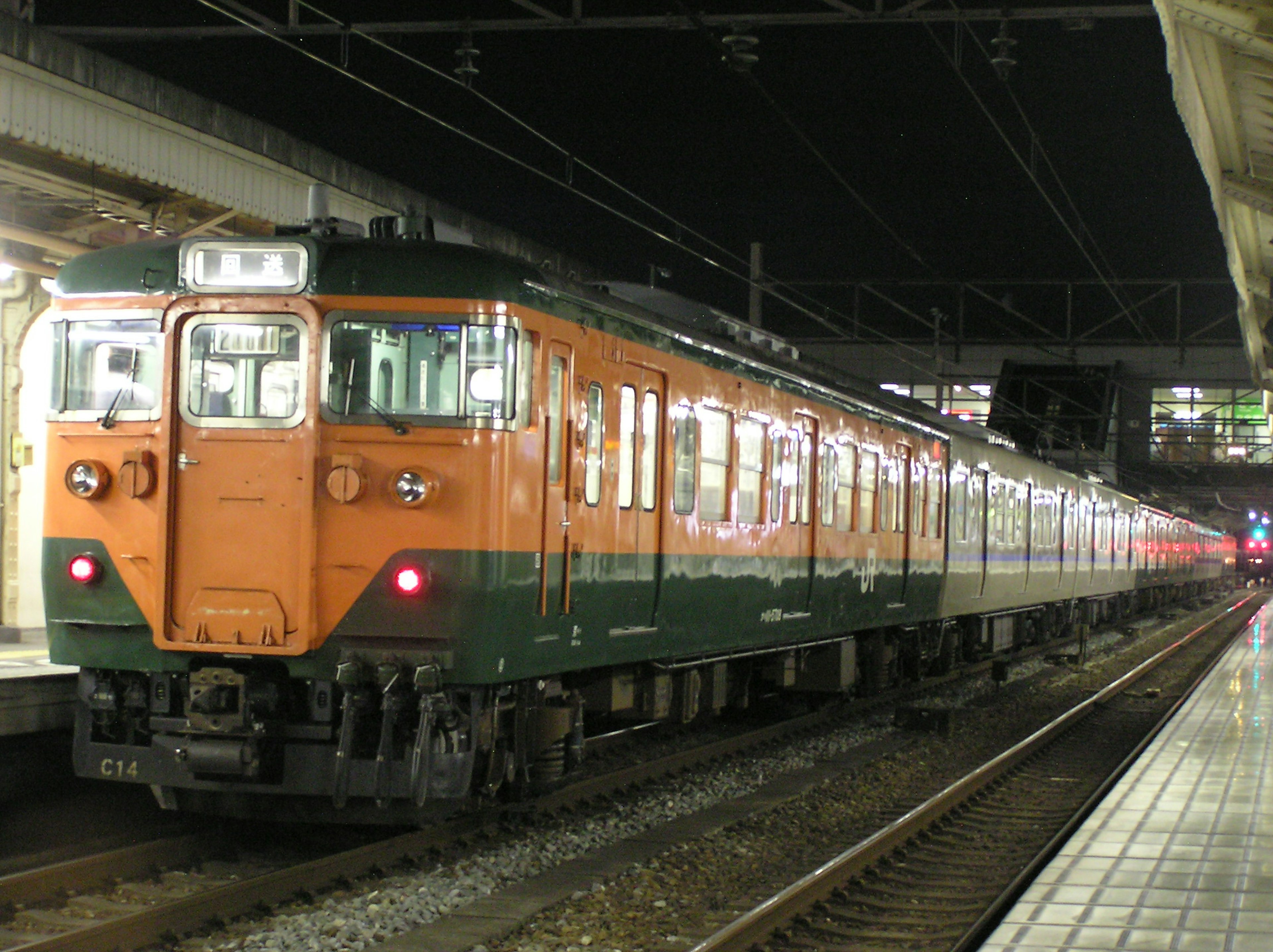 Tren naranja y verde detenido en una estación de noche