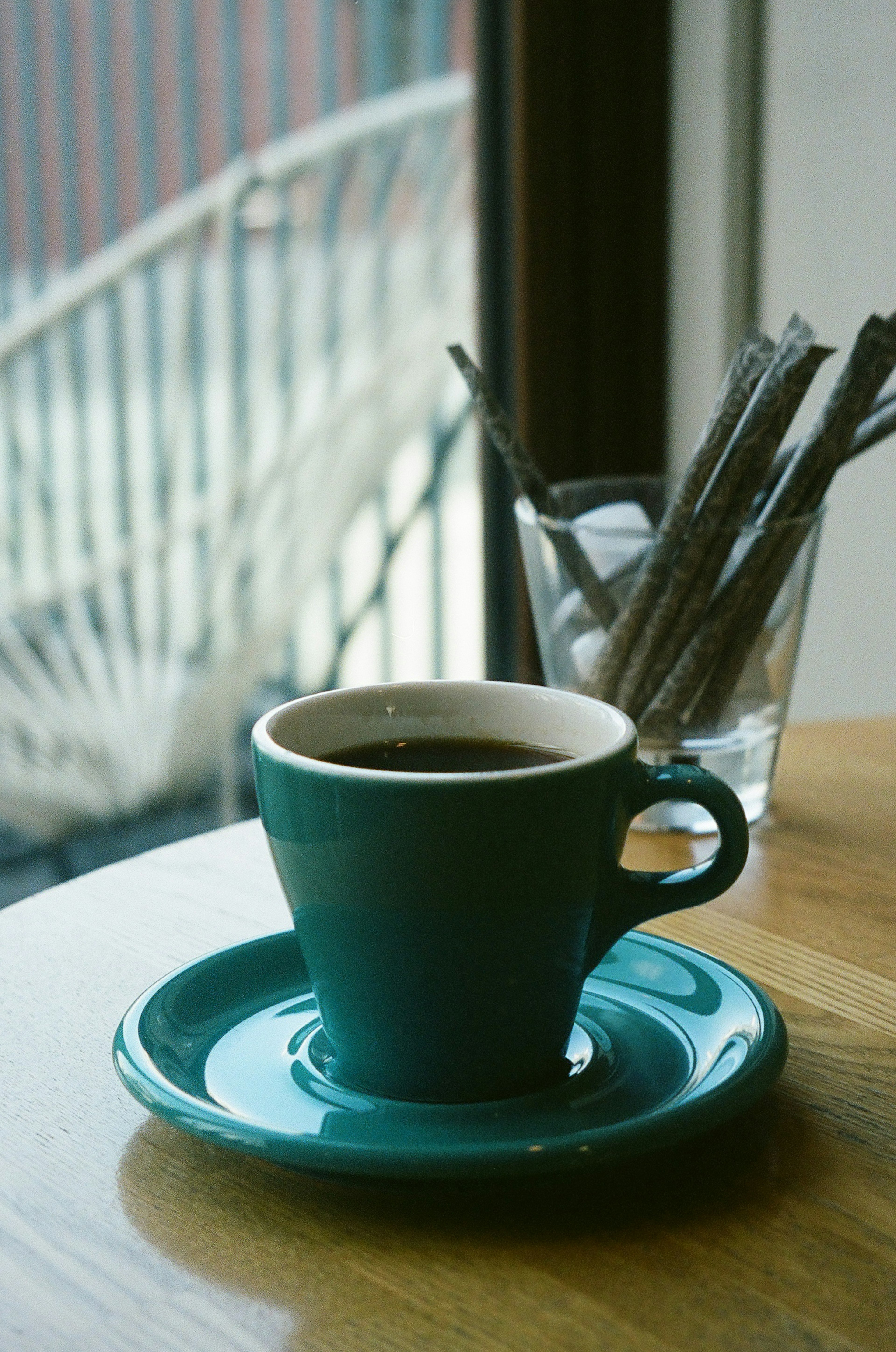 Blauer Kaffeebecher auf einem Holztisch mit Unterteller und einem Glas mit Strohhalmen