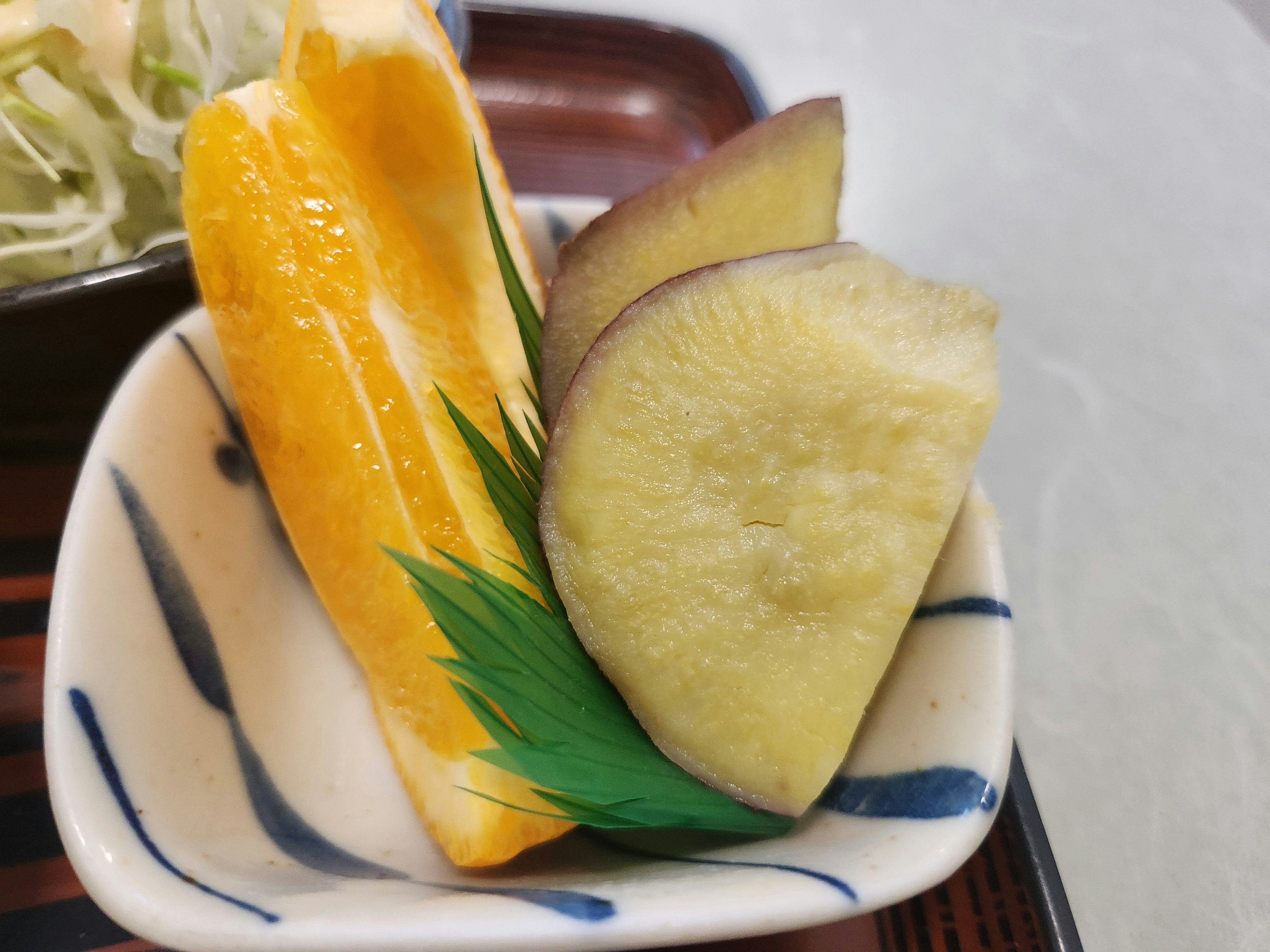 A small dish with yellow kamaboko and purple sweet potato garnished with green leaves