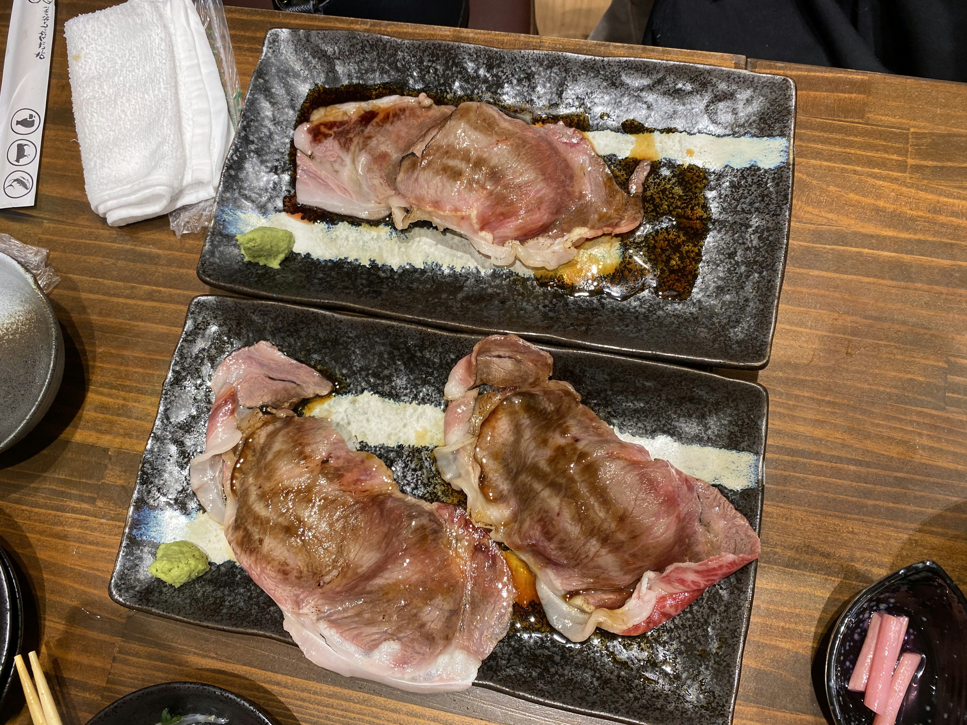 Zwei Teller mit gegrilltem Fleisch auf schwarzen Tellern auf einem Holztisch