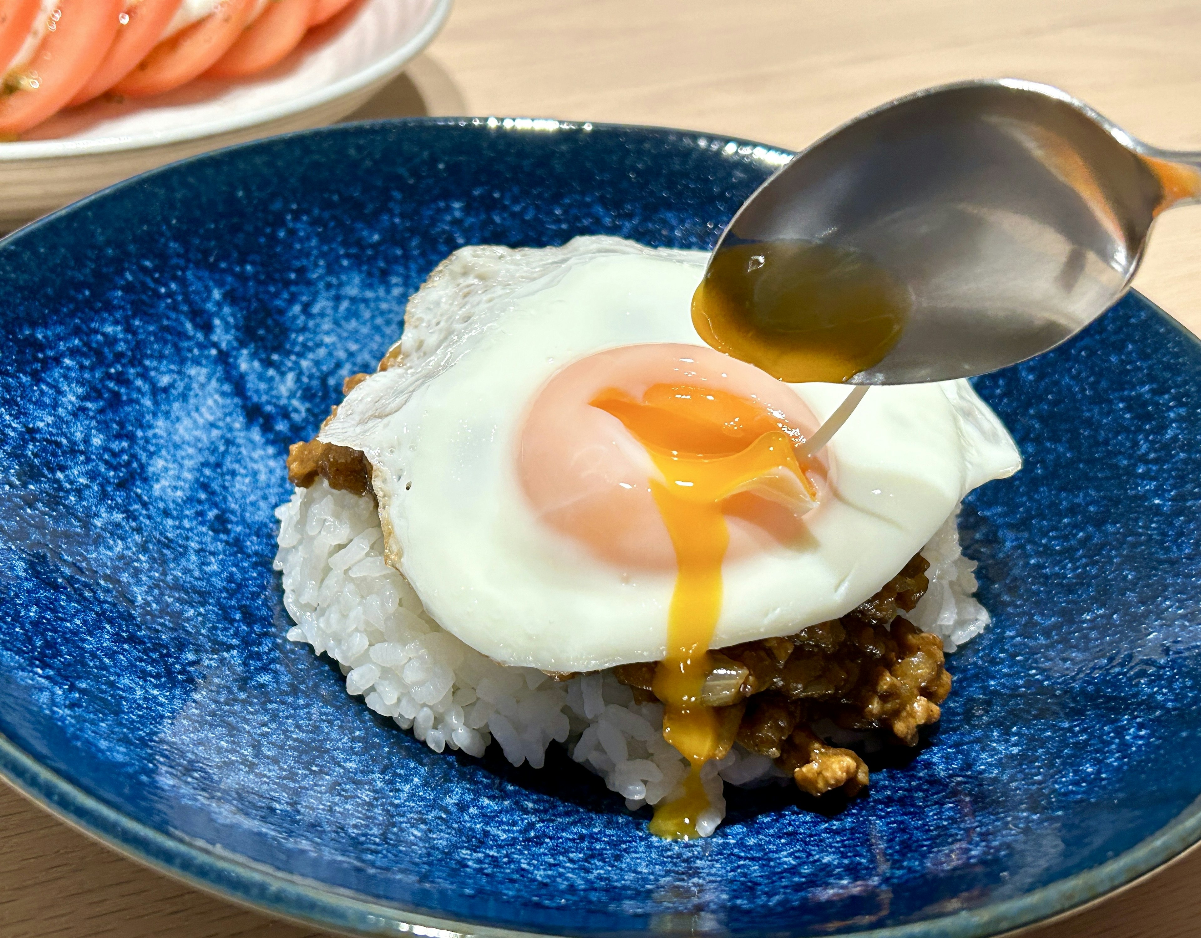 青い皿に盛られたご飯の上に半熟卵が乗っている料理