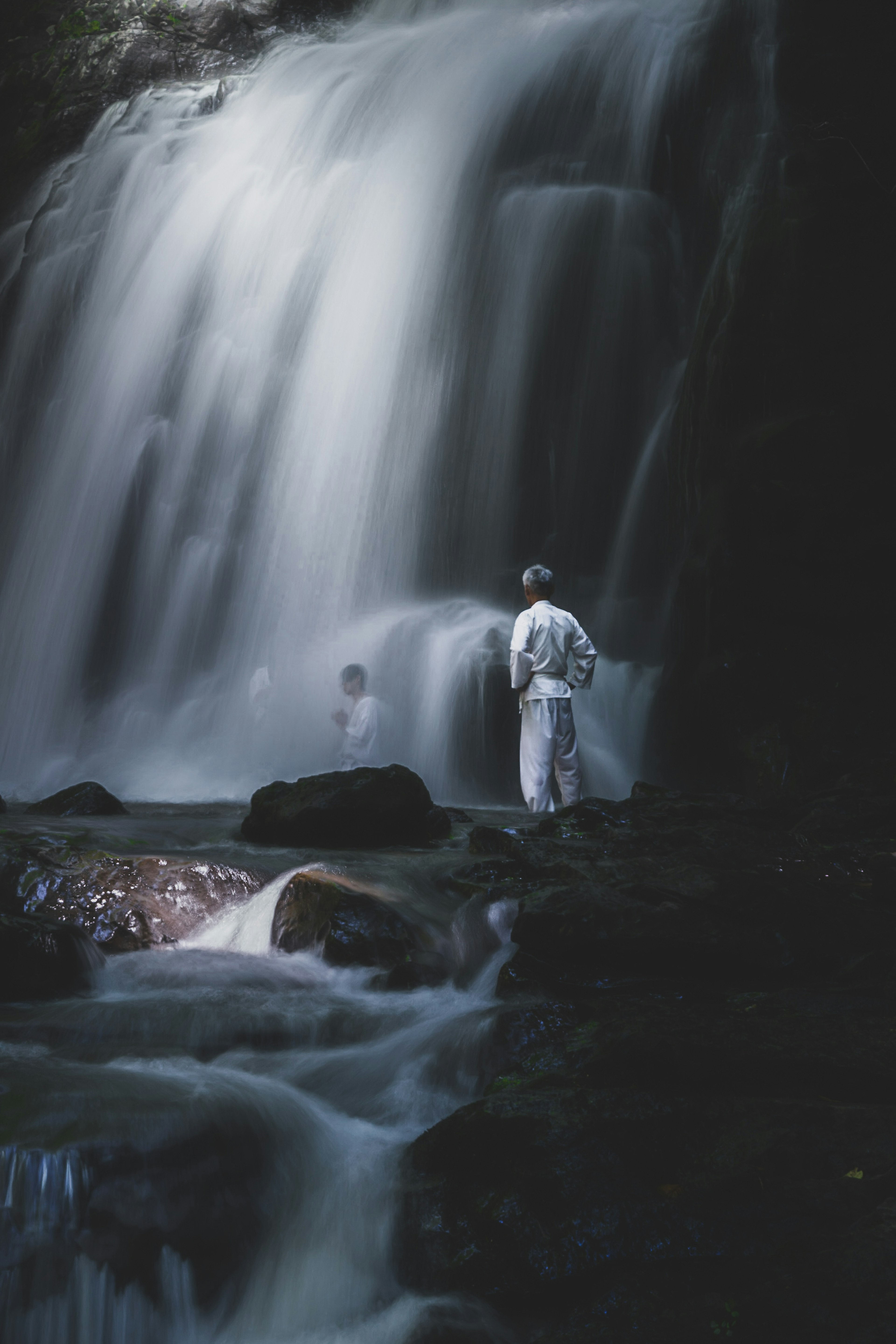 滝の前に立つ白い衣装の人物と水の流れ