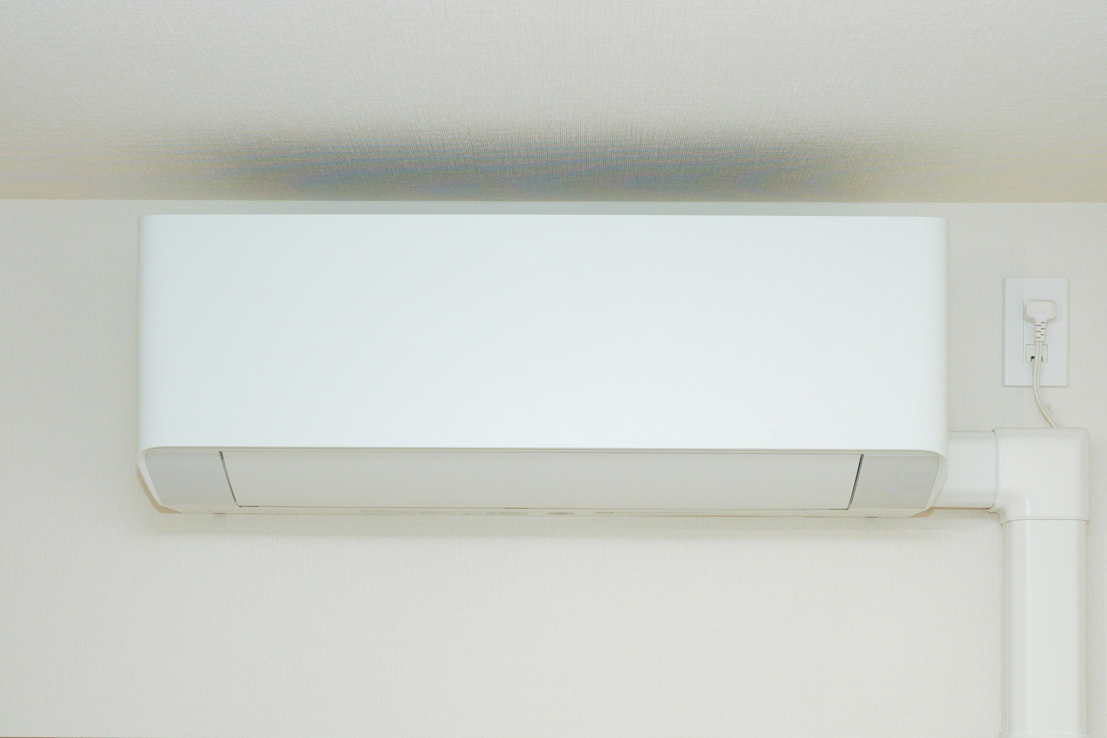 A white air conditioning unit mounted on the ceiling in a simple indoor setting