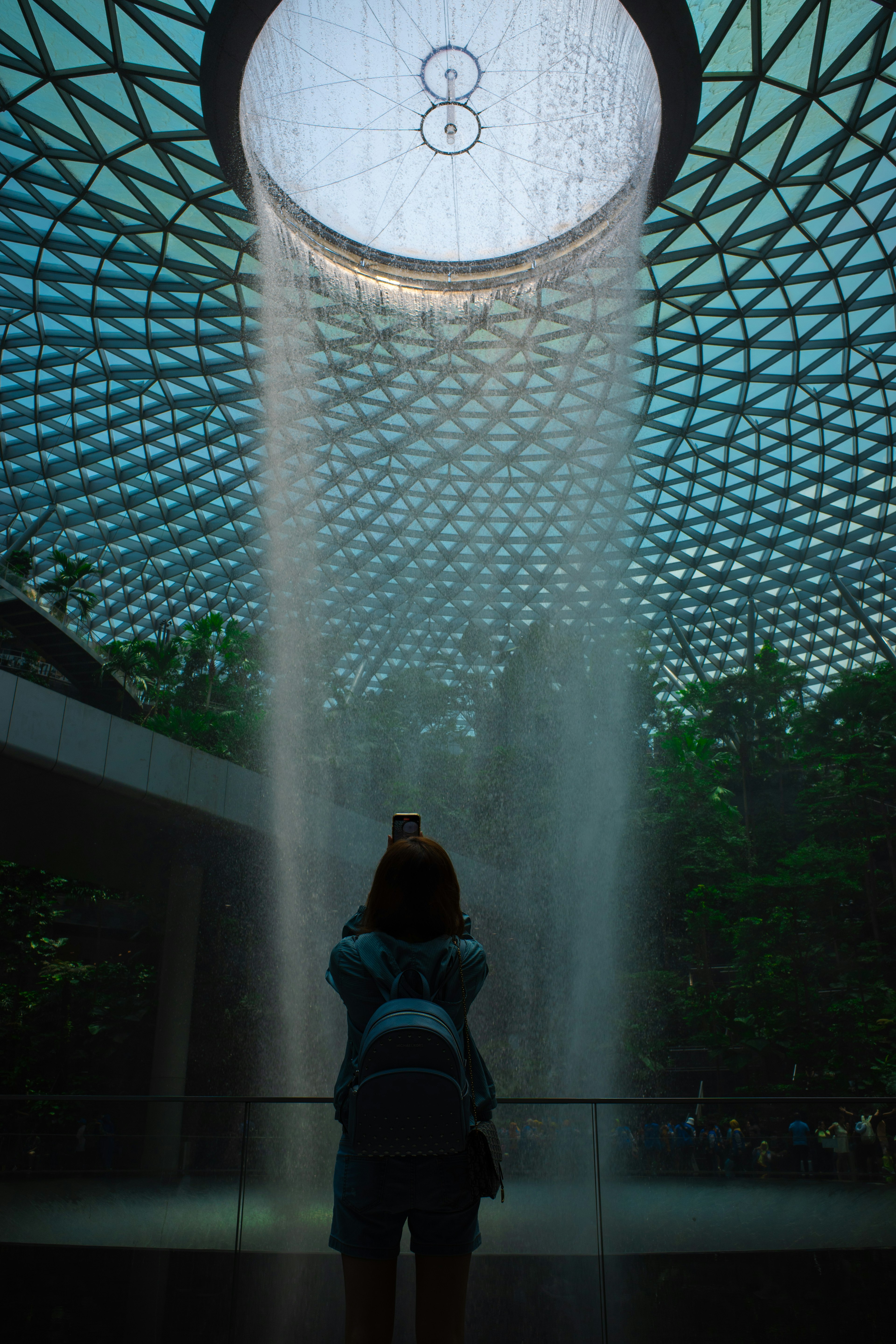 Visitor taking a photo in Jewel Changi Airport with a waterfall and unique architectural design