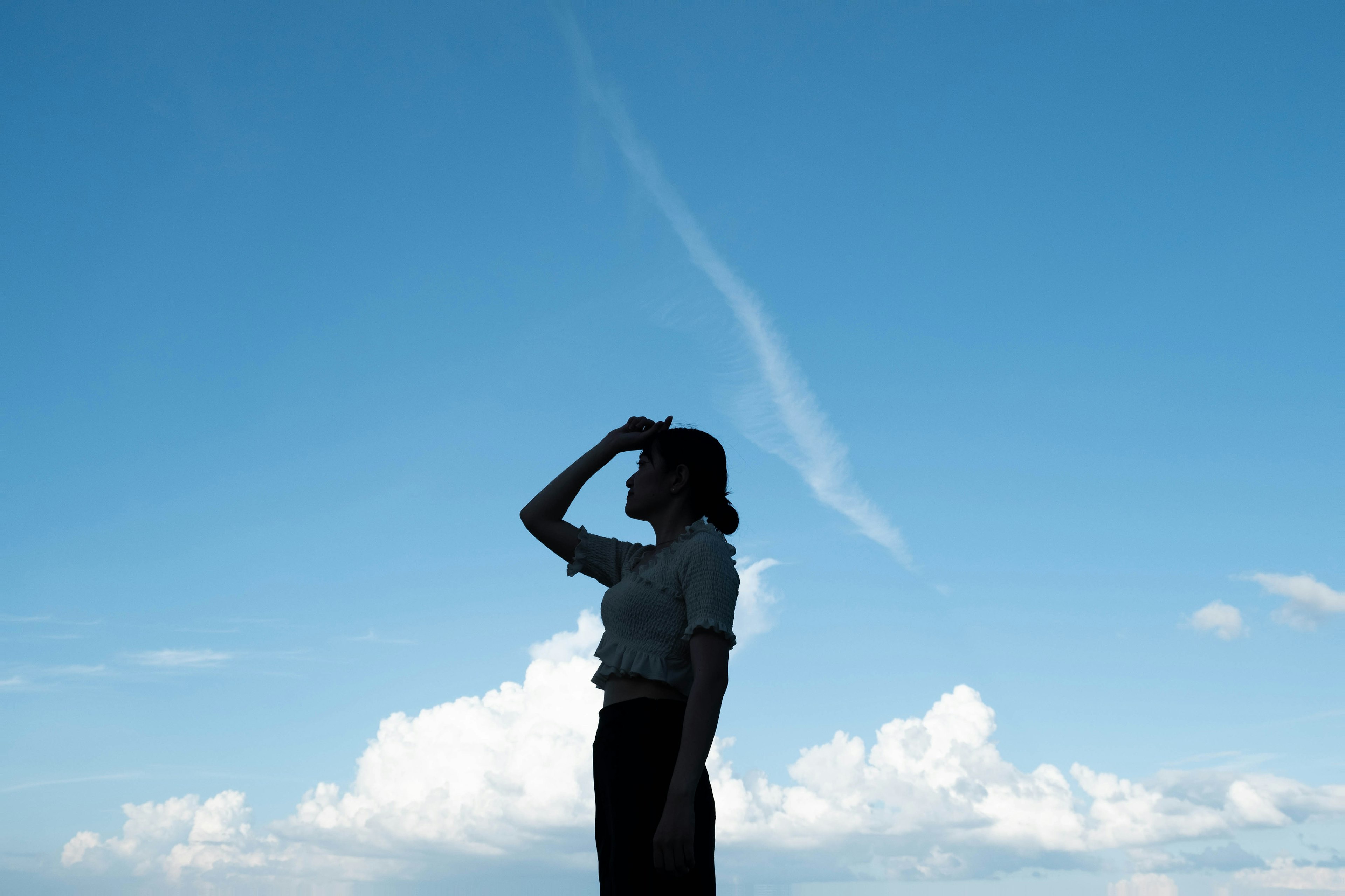 青空の下で手を額にかざしている女性のシルエット