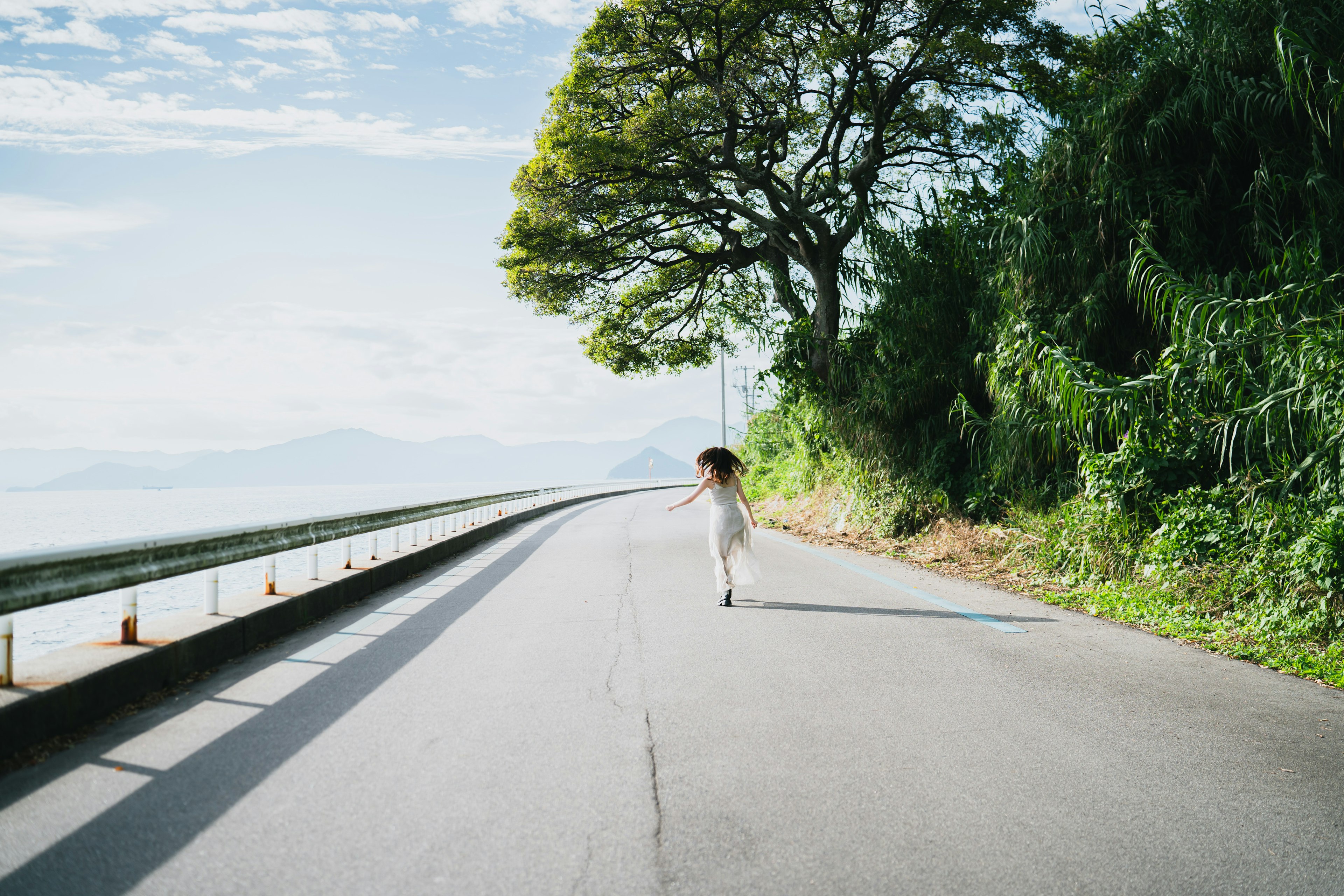 海に沿った道路を走る女性と青空の景色