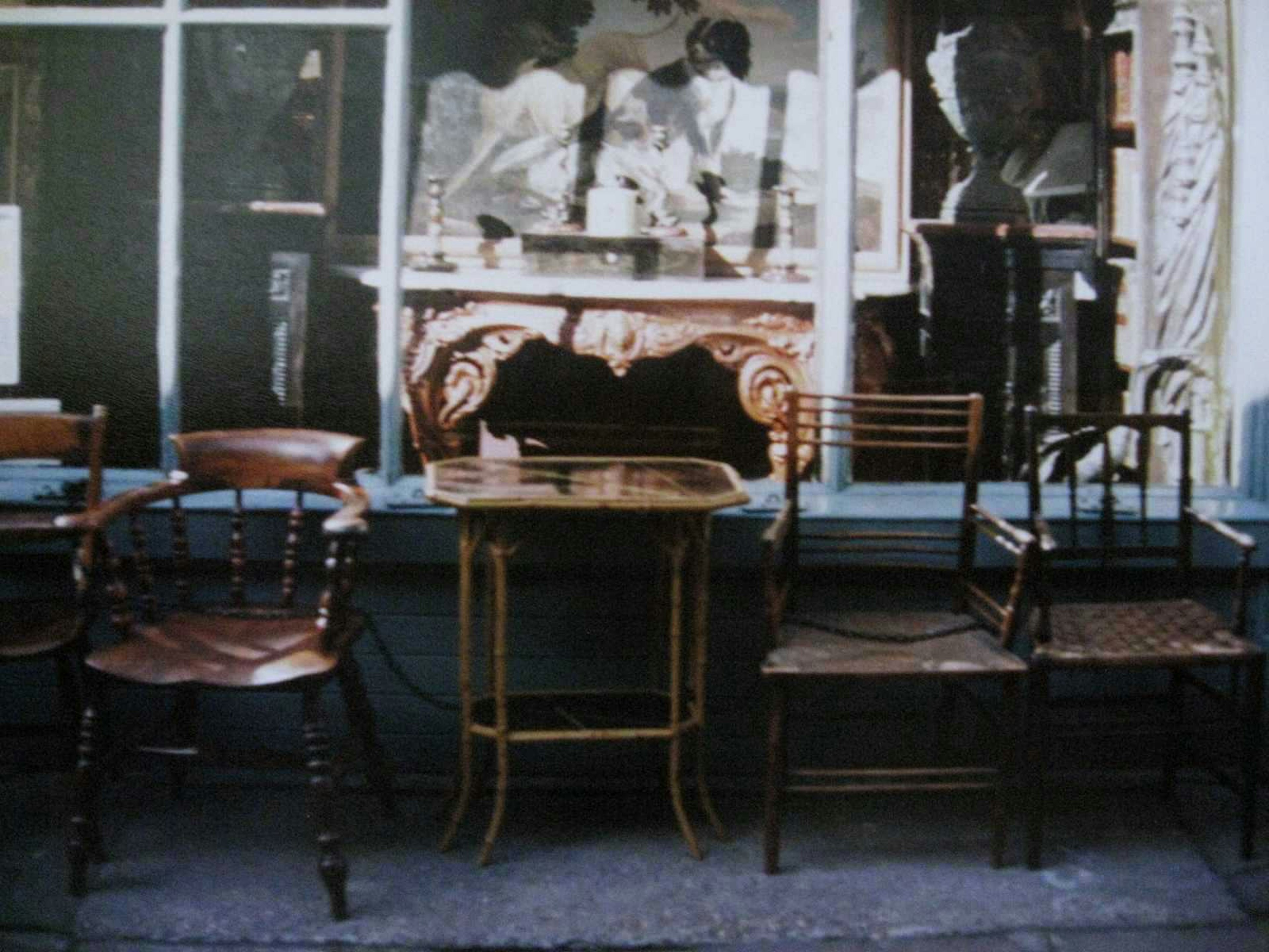 A row of vintage chairs outside a café wooden chairs and a table reflected in the café's window