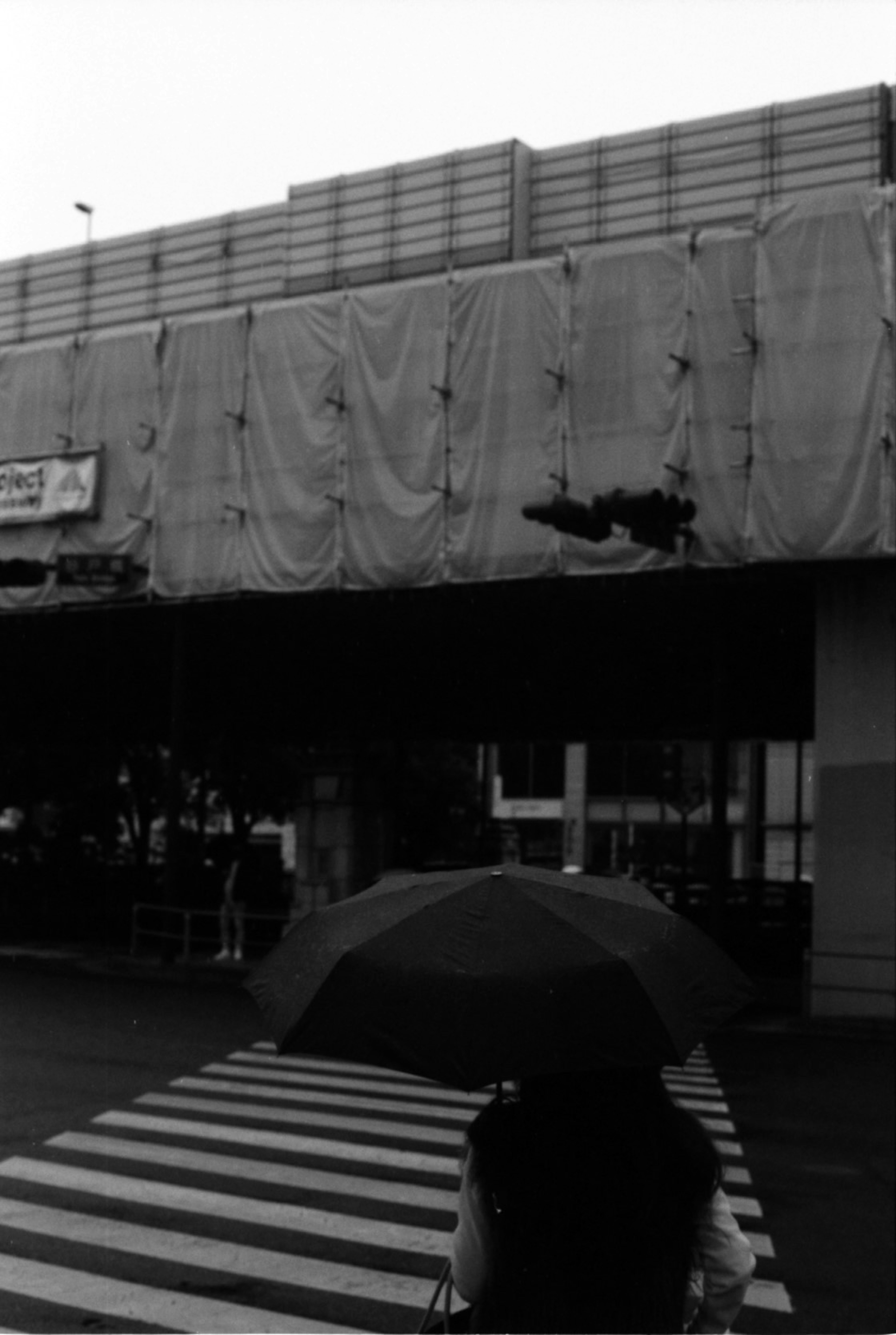 Photo en noir et blanc montrant une personne avec un parapluie et un passage piéton devant un chantier