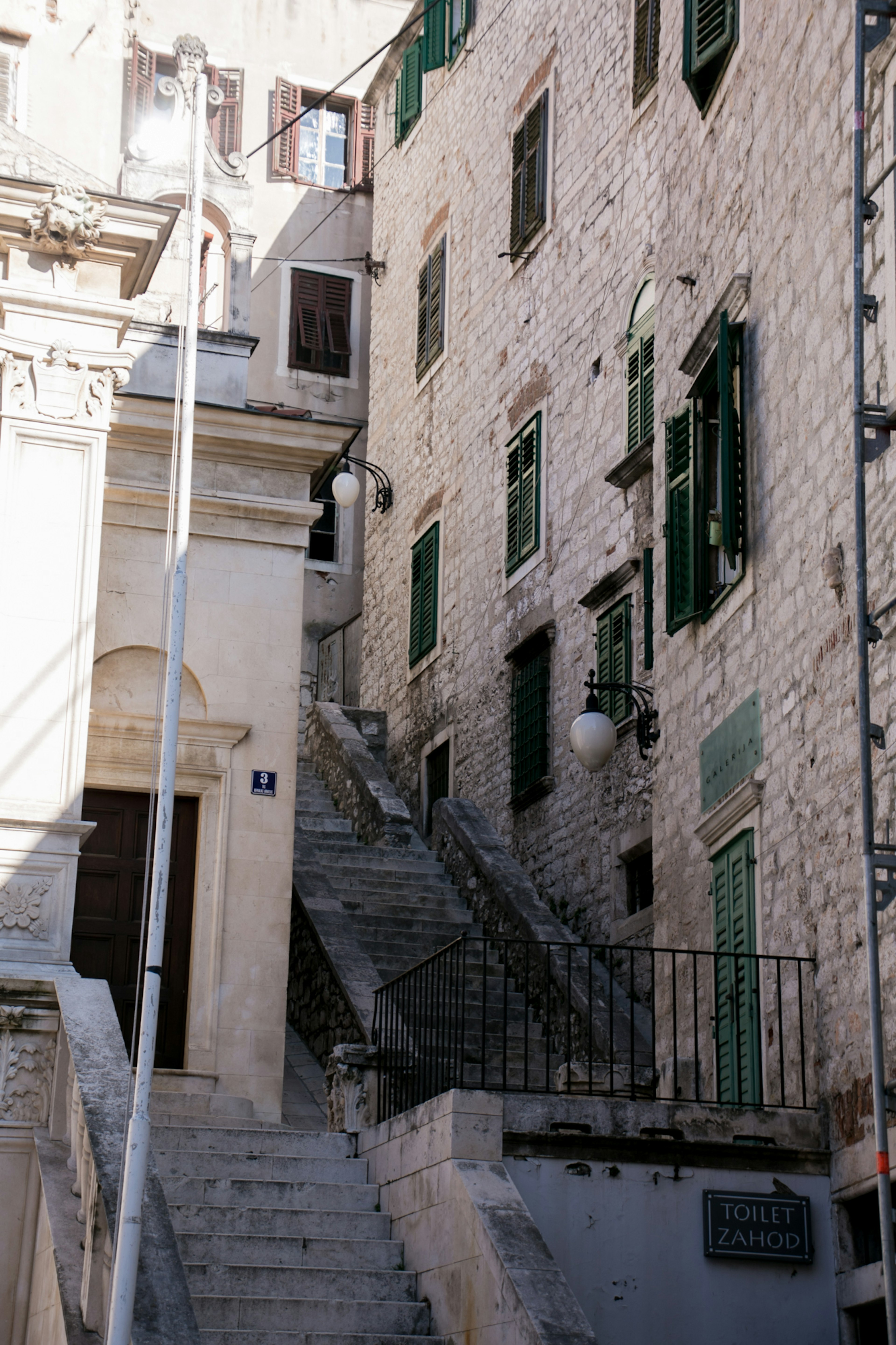 Edificios de piedra con marcos de ventanas verdes y una escalera en un callejón estrecho