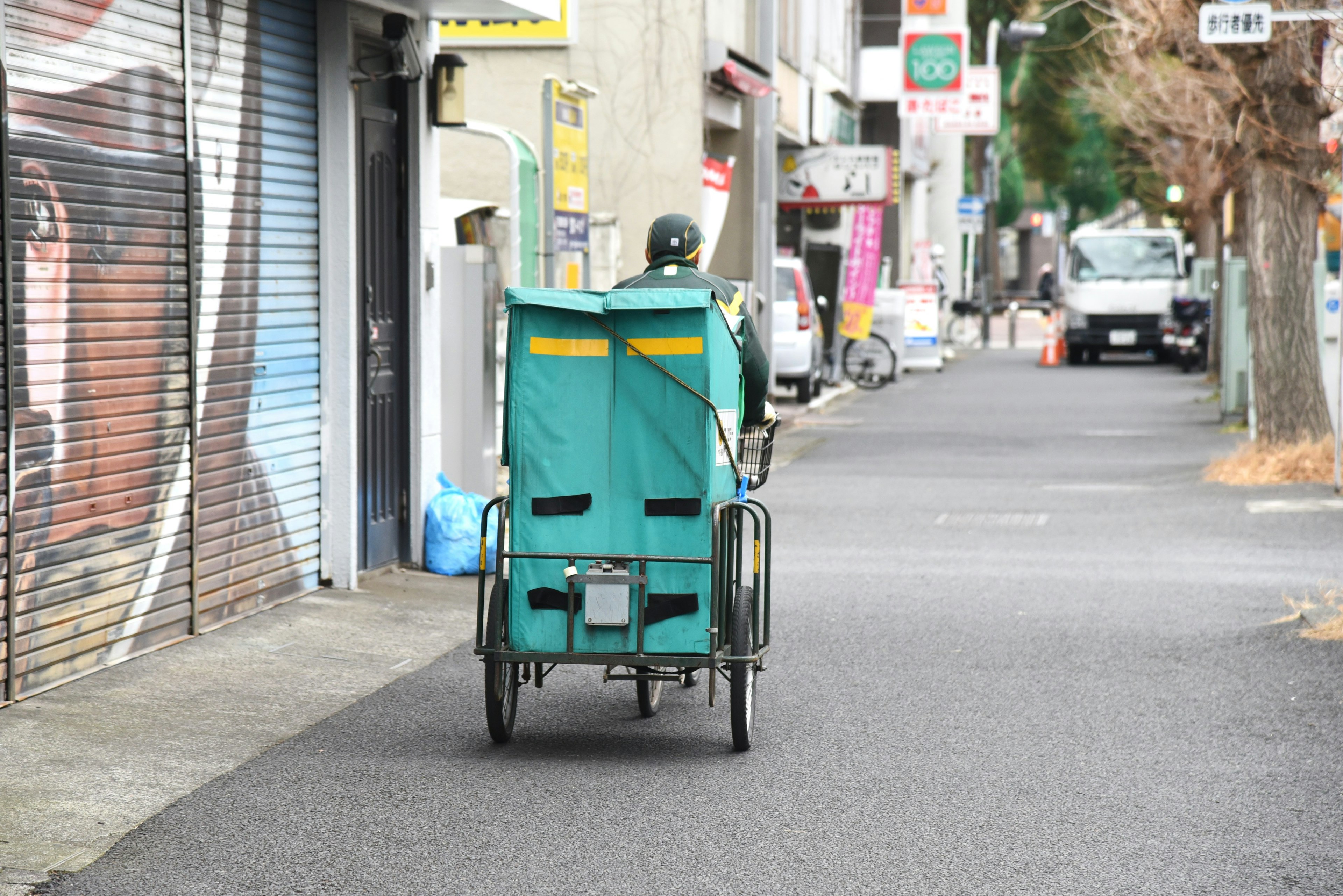 Sebuah becak hijau melaju di jalan sempit dengan pengemudi terlihat dari belakang