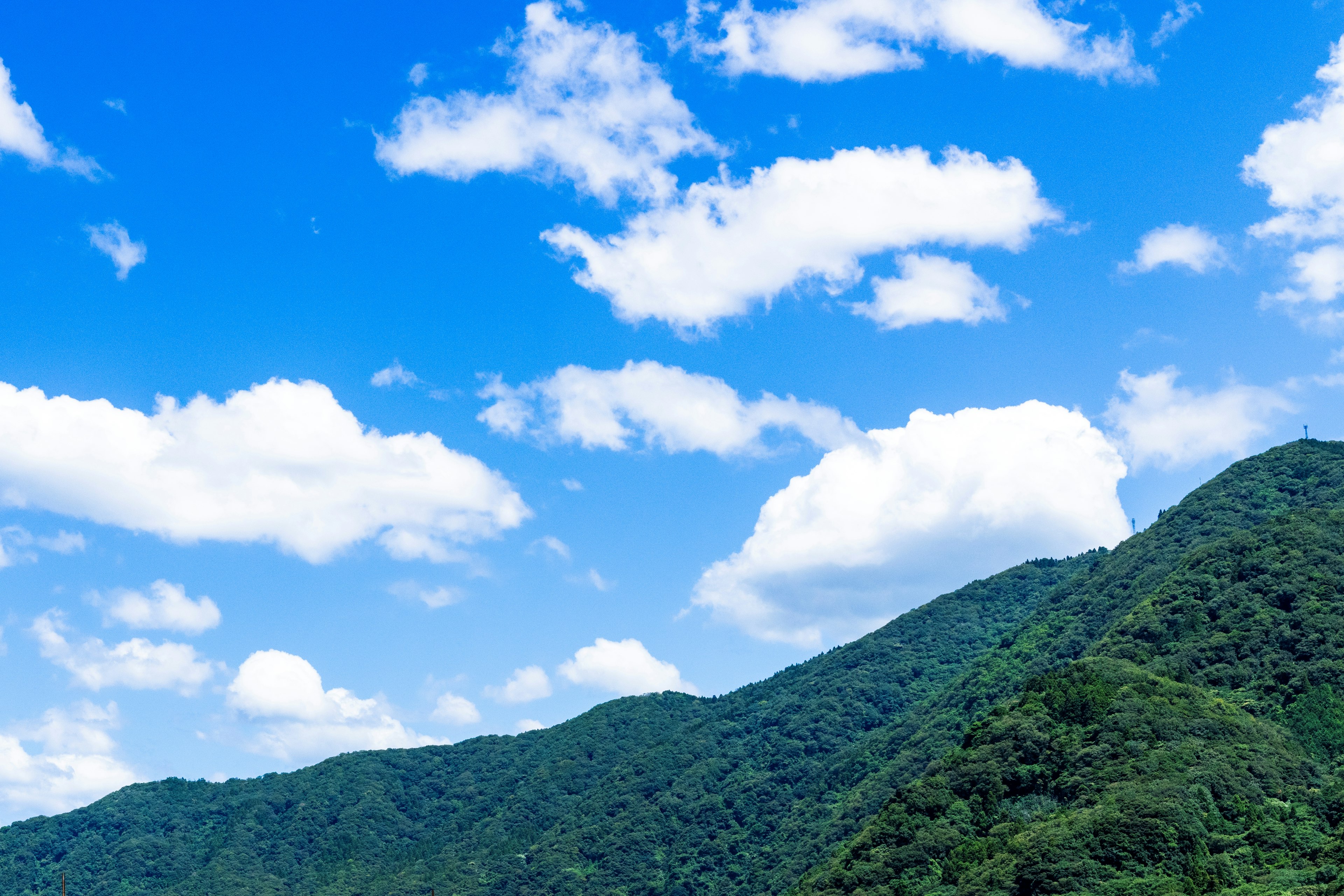 Lush green mountains under a bright blue sky with fluffy white clouds