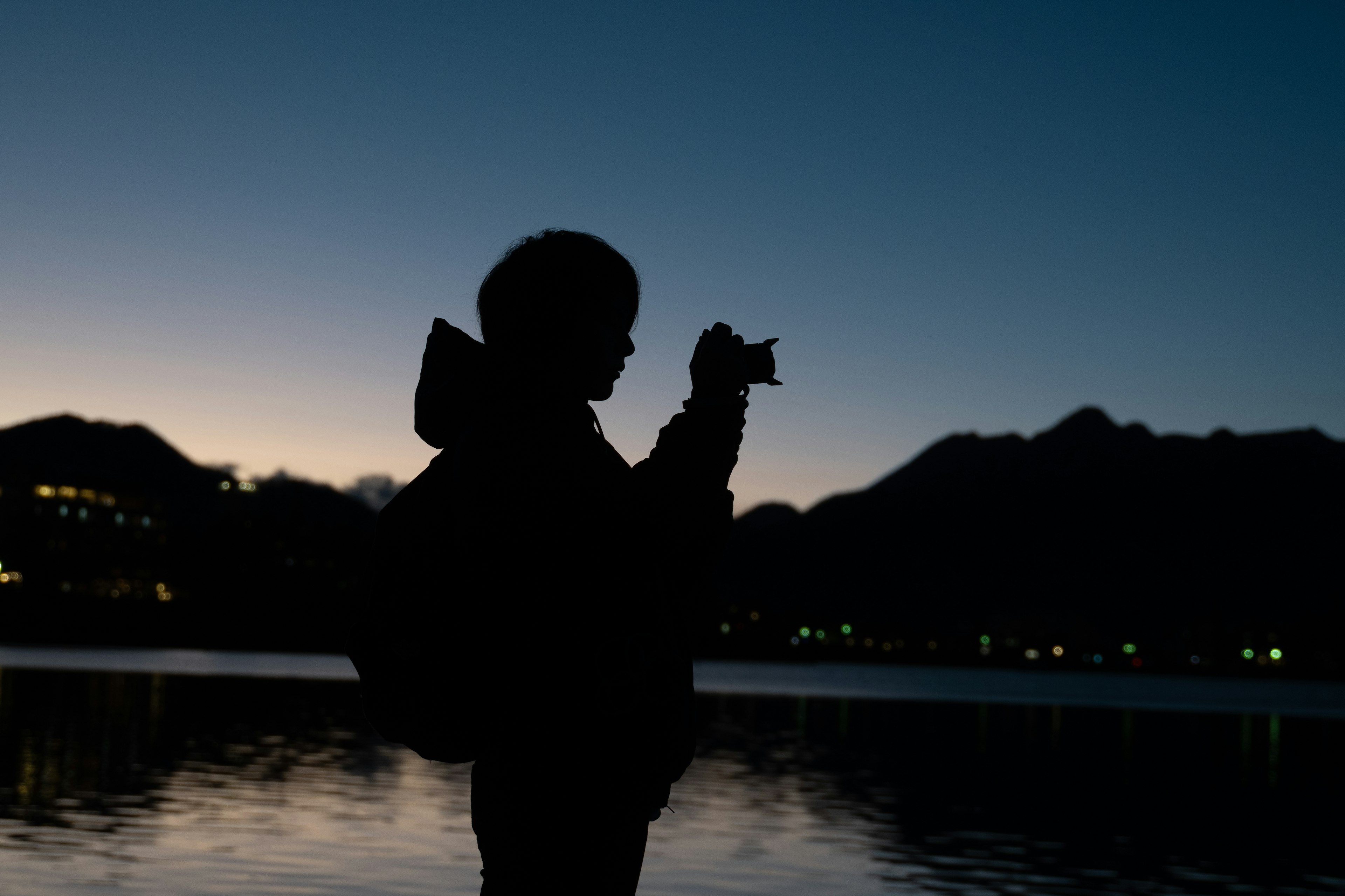 Silhouette of a person holding a camera at dusk with mountains in the background