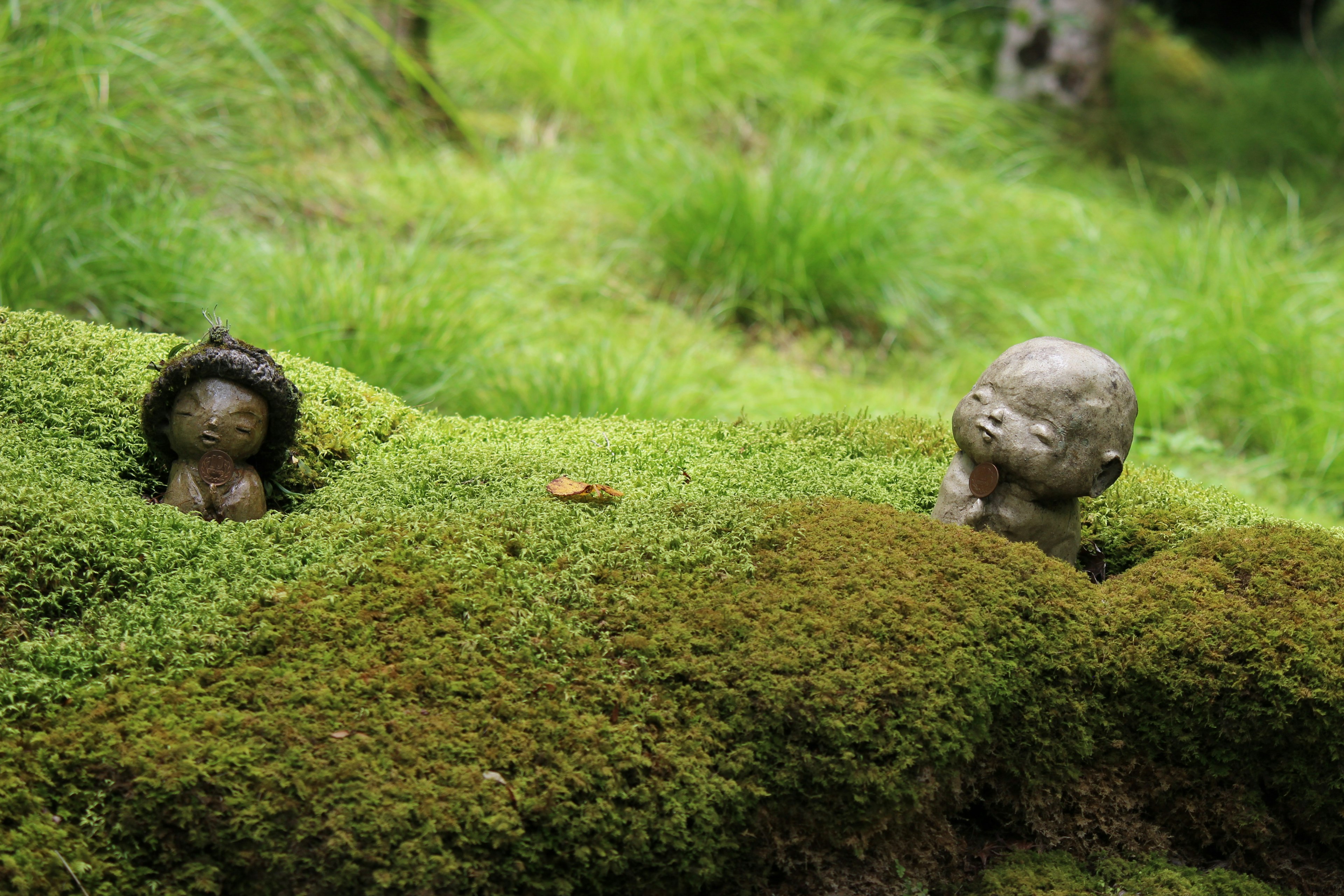 Two small sculptures nestled in mossy ground surrounded by greenery