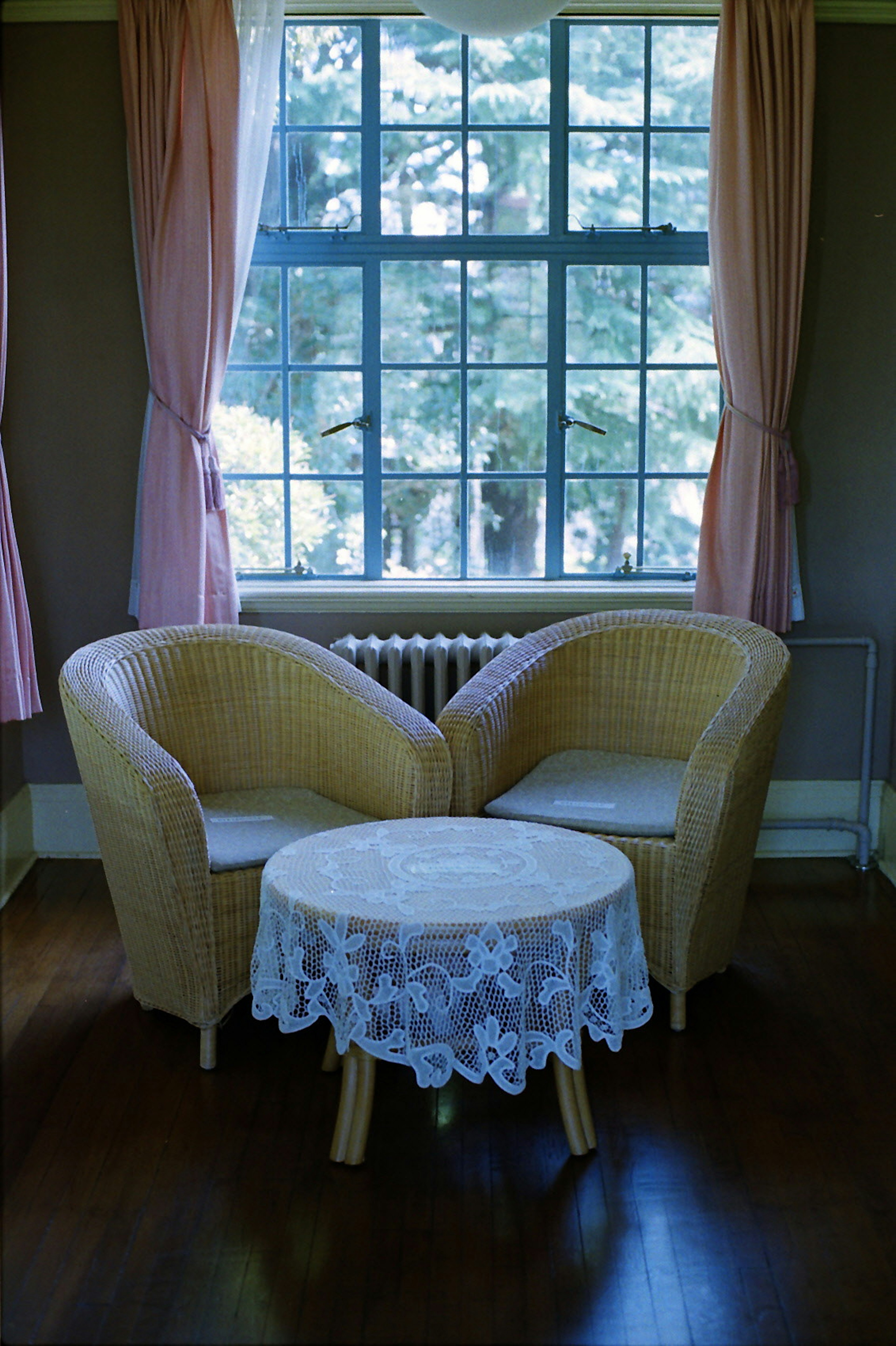 Two rattan chairs and a lace-covered table near a window