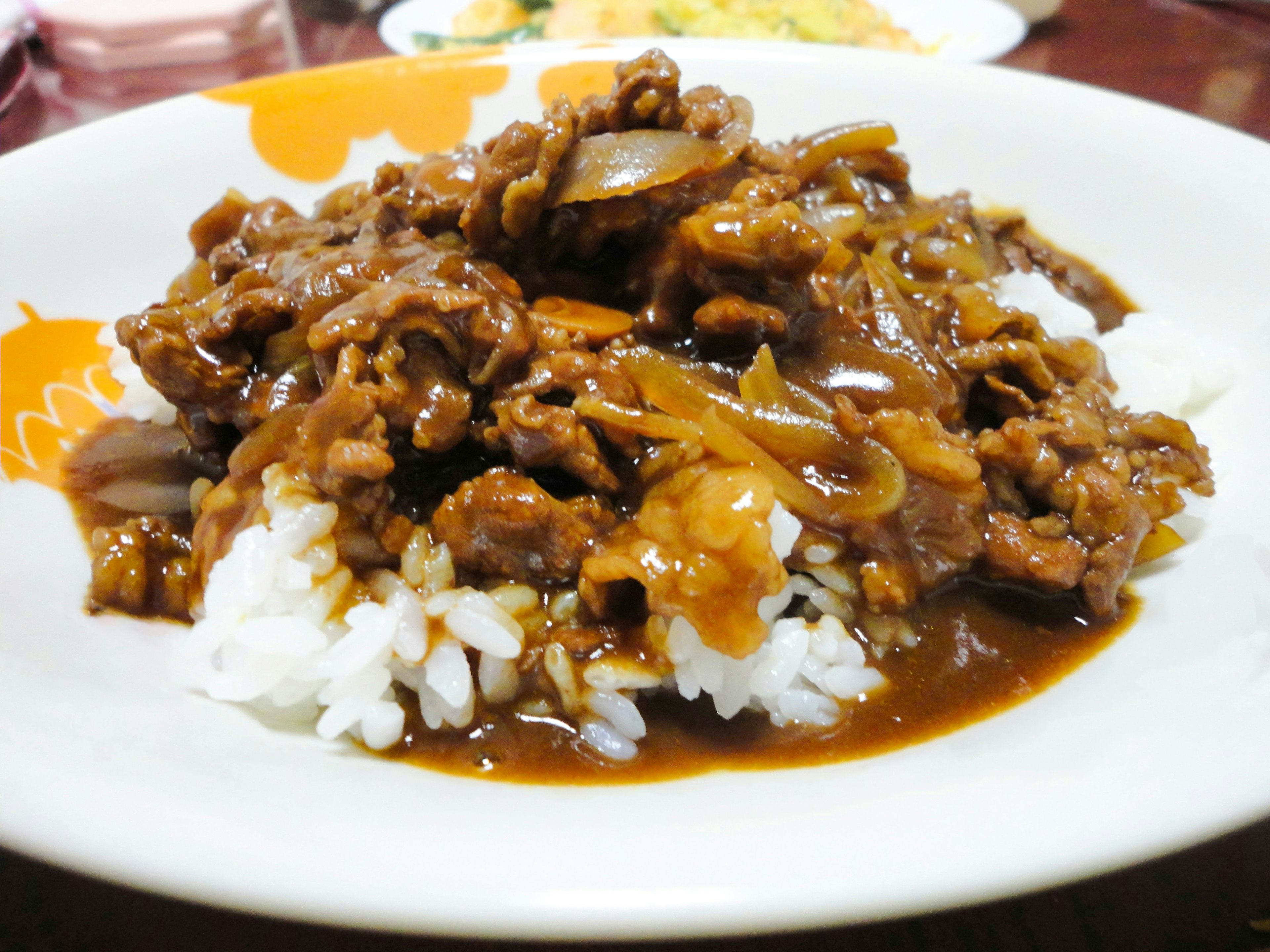 Dish featuring beef and onions in a sweet and savory sauce served over rice