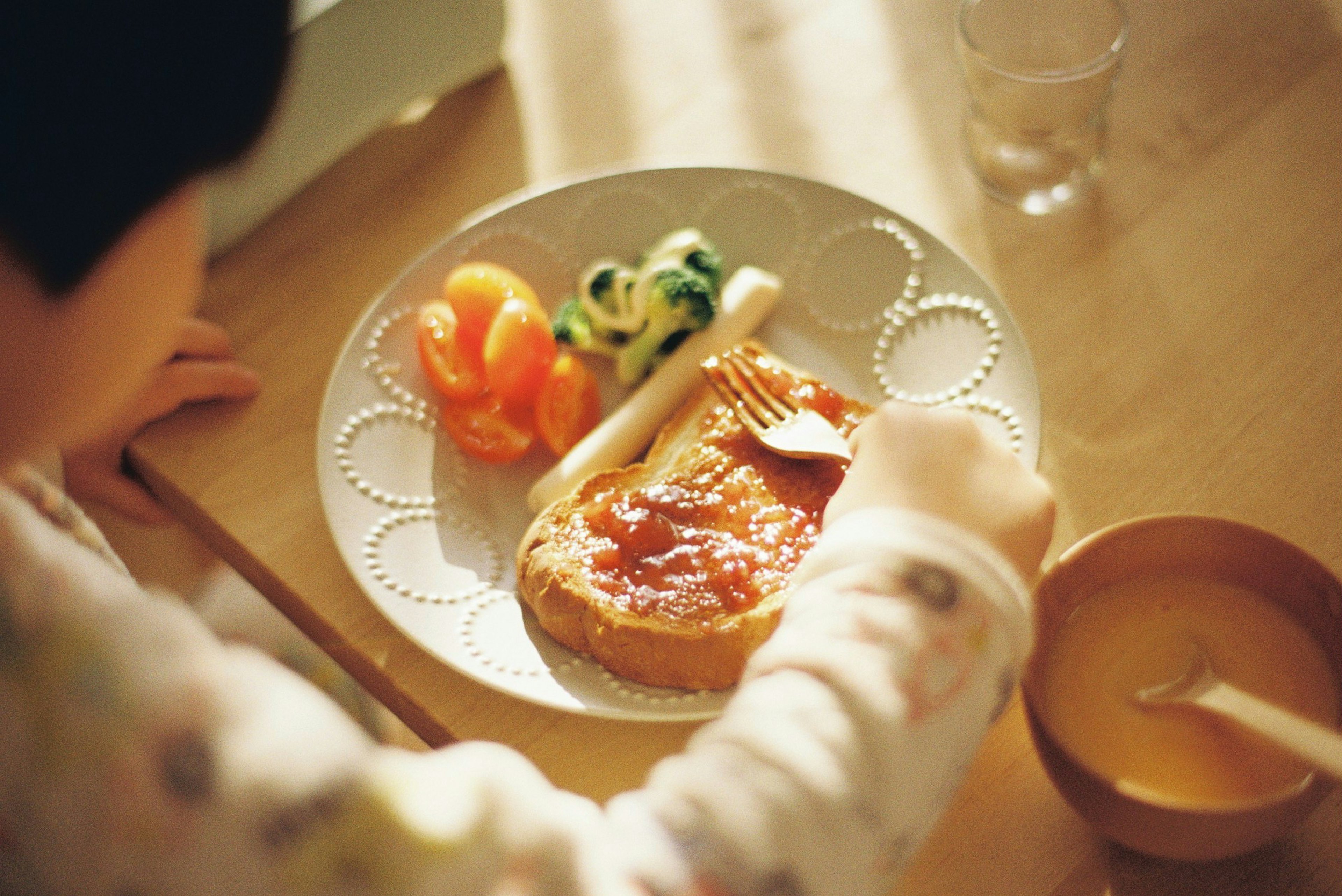 子供がジャムを塗ったパンを食べる様子と野菜のサラダ