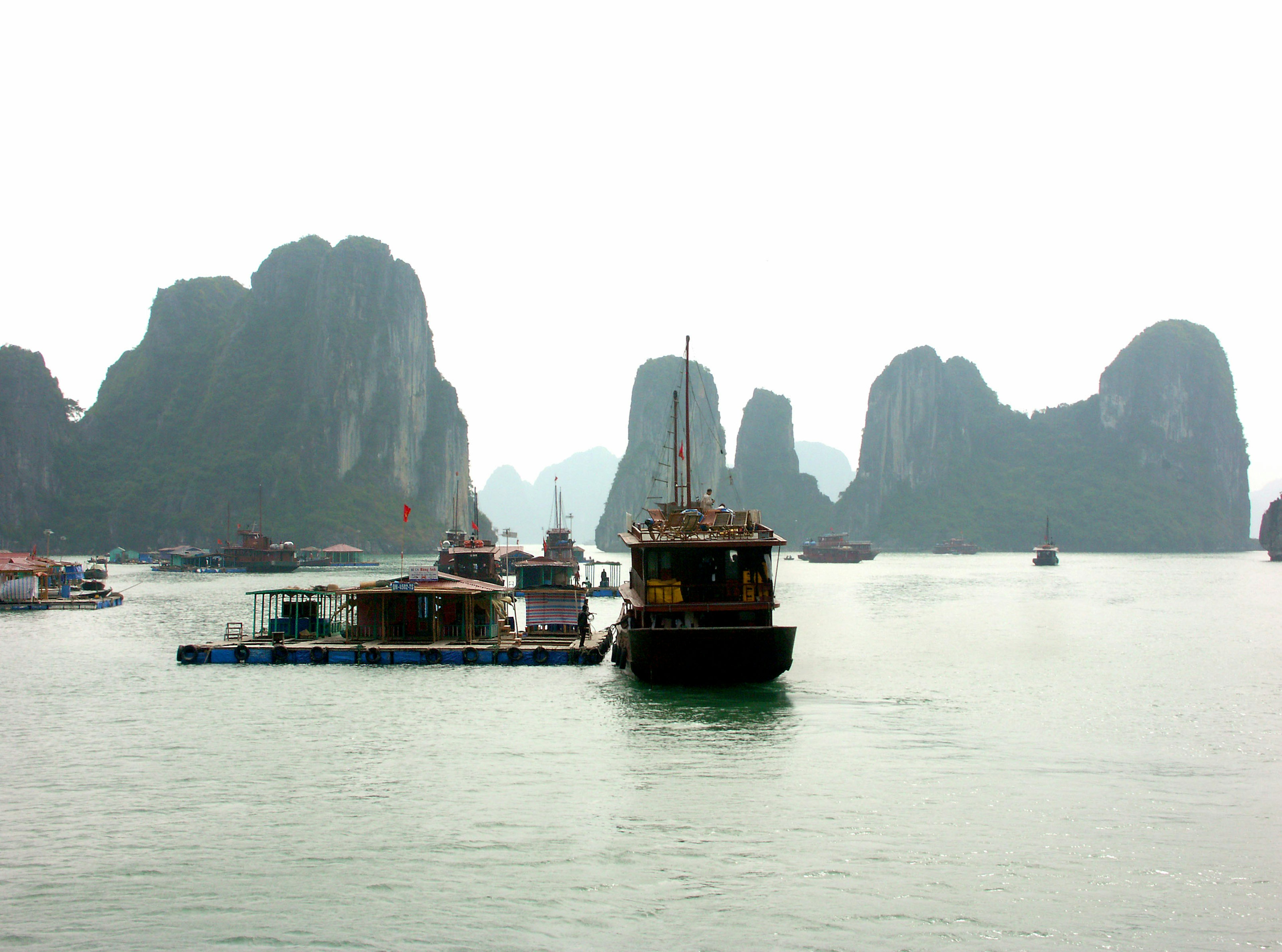 Karst di calcare nebbiosi e barche nella baia di Ha Long