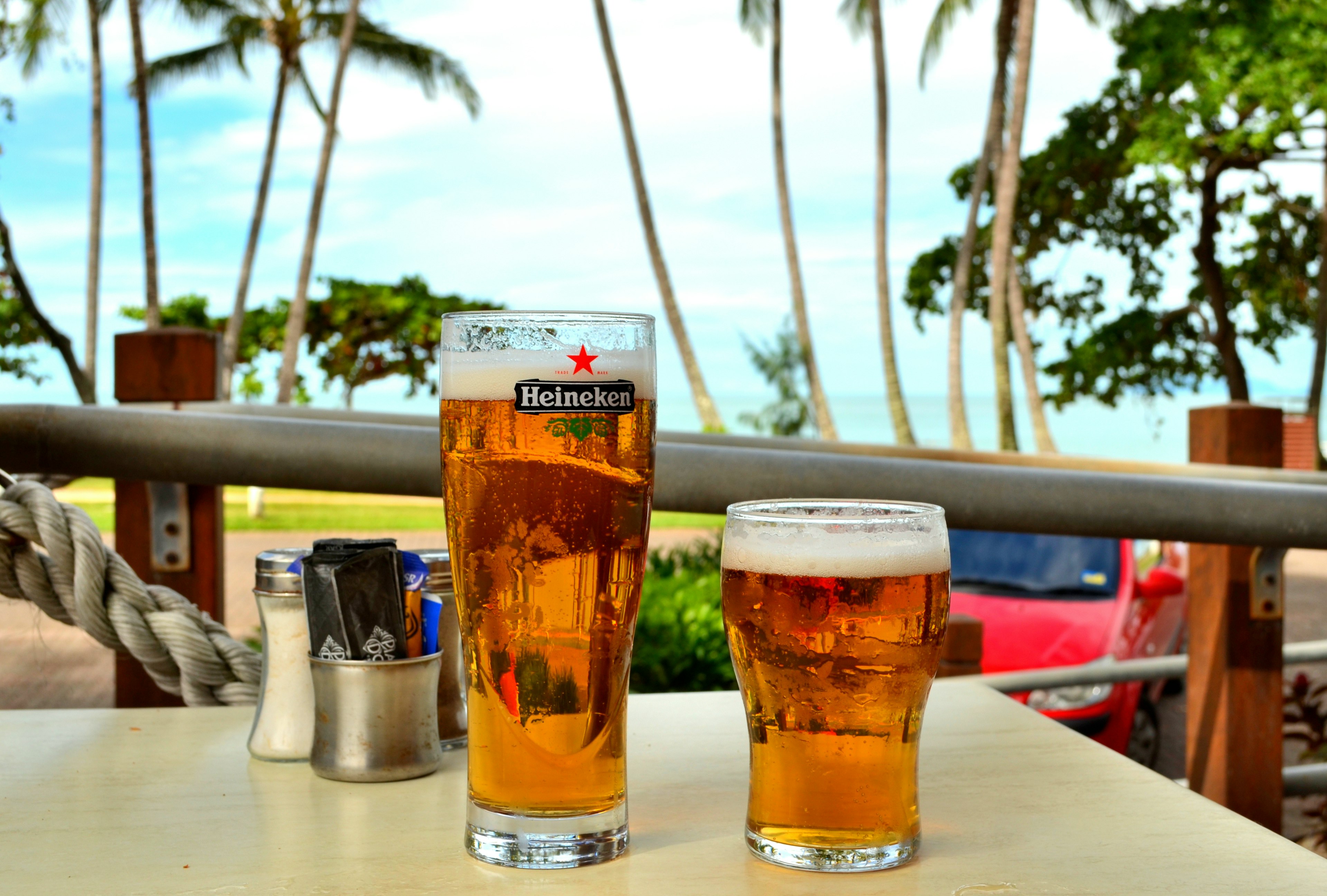 Due bicchieri di birra su un tavolo con vista sulla spiaggia e palme sullo sfondo