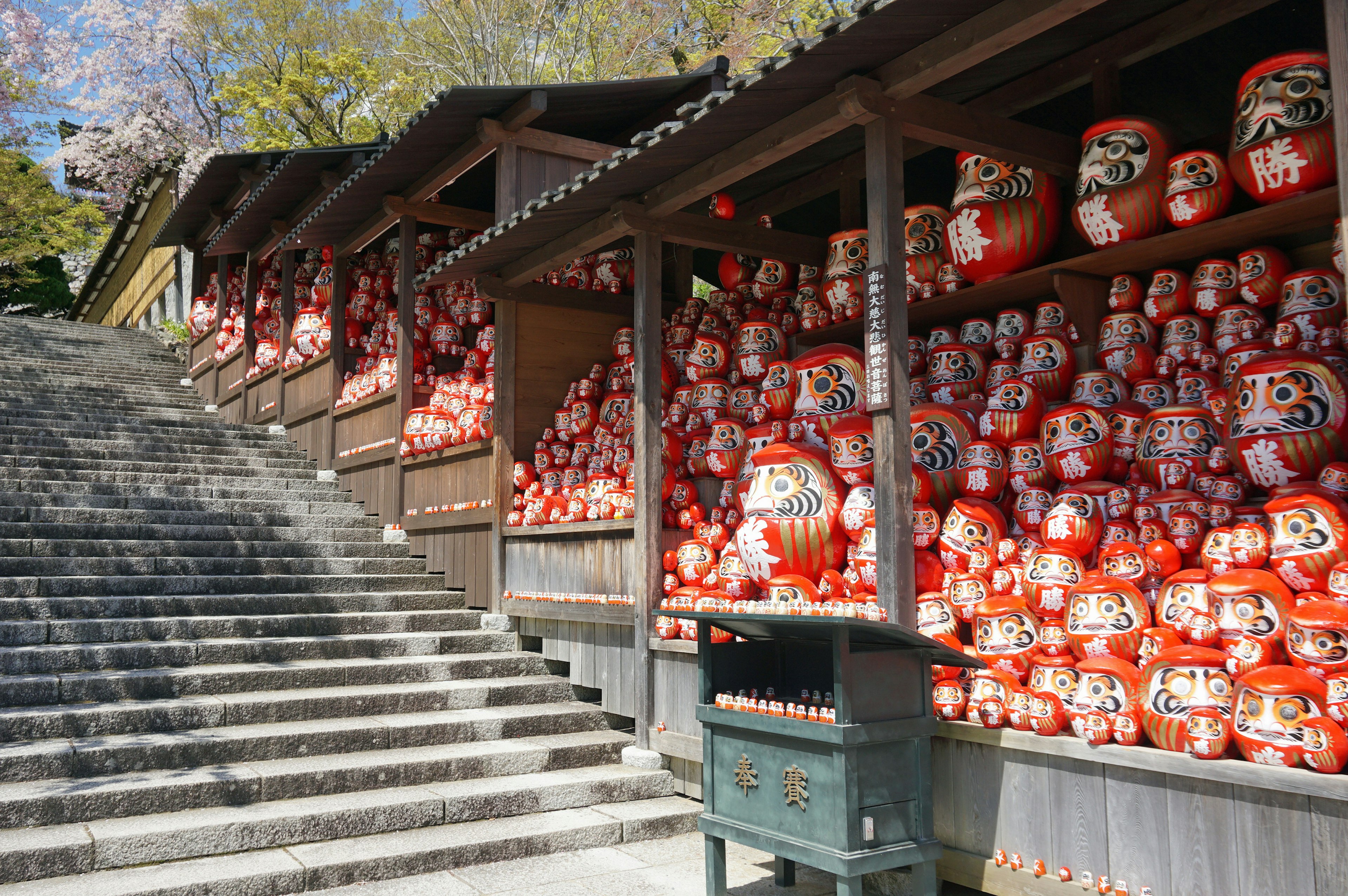 Escaleras alineadas con muñecas Daruma rojas bajo refugios de madera