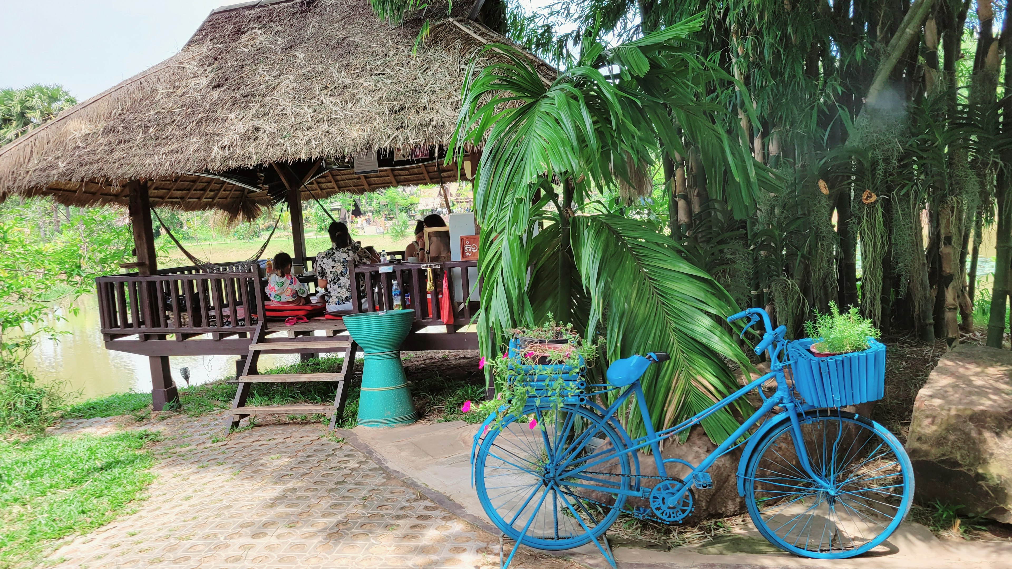 Rural scene featuring a blue bicycle and a thatched-roof pavilion