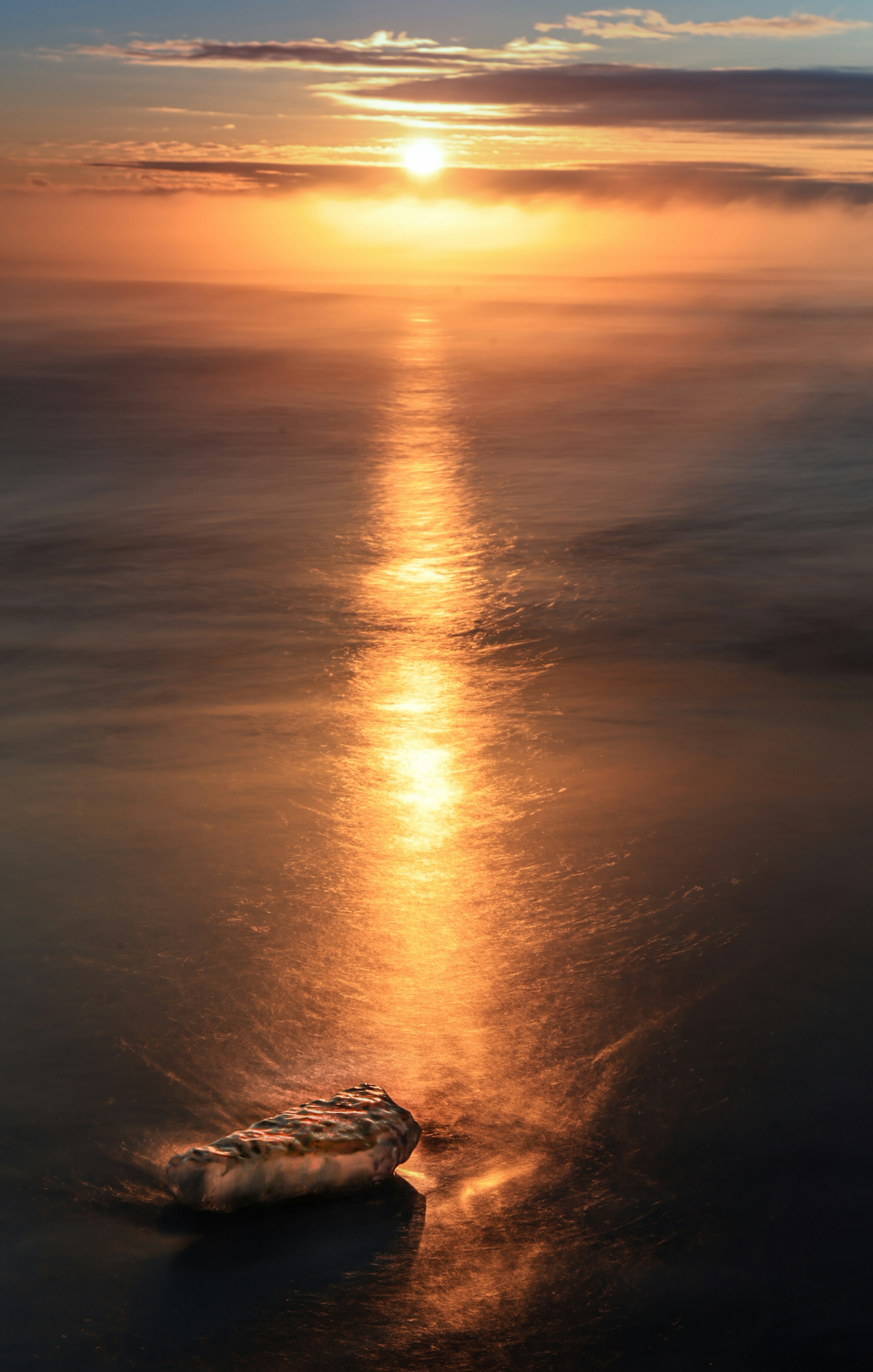 Stunning sunset reflecting on the ocean with orange light spreading across clouds and calm water