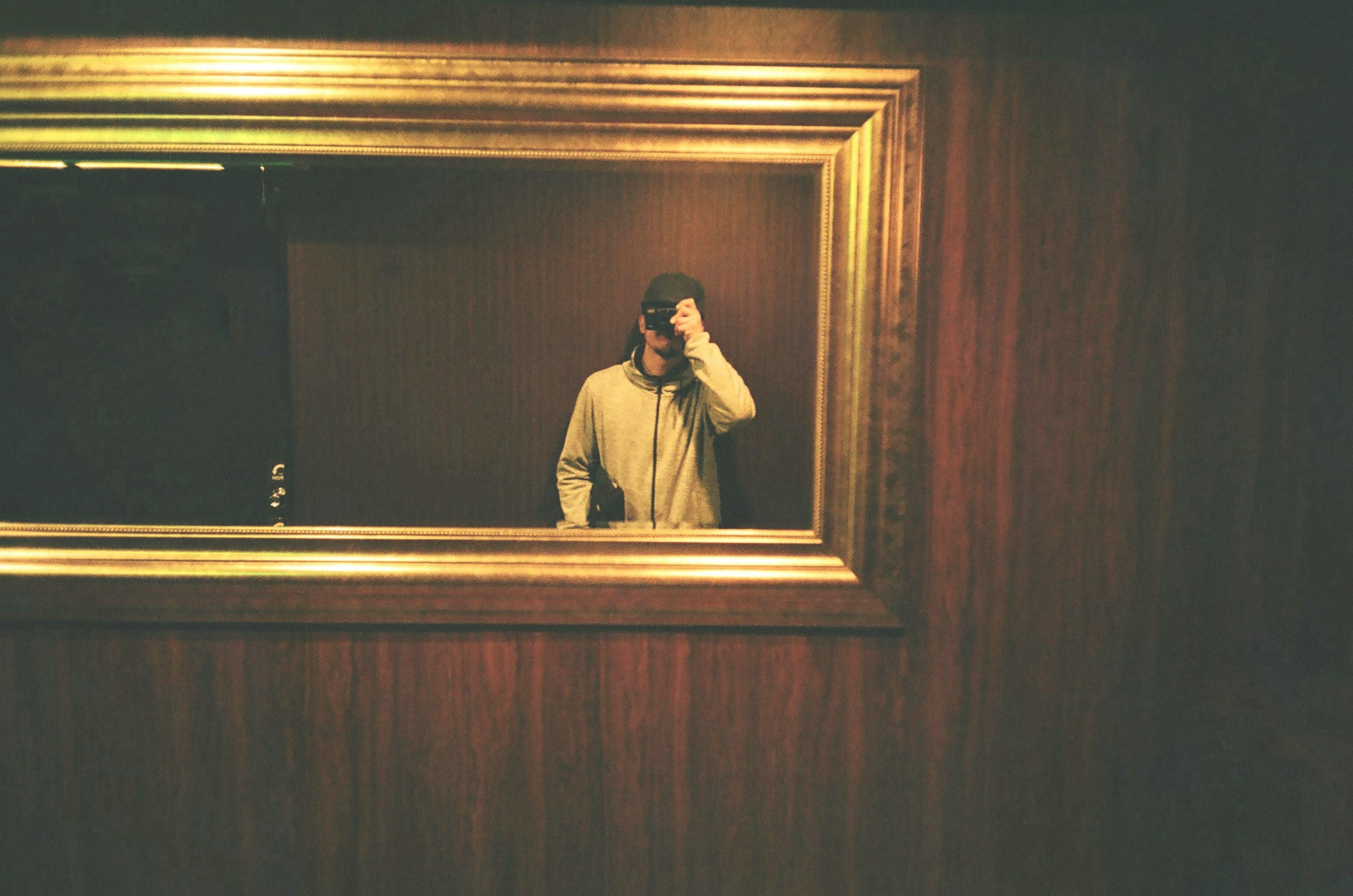 A person standing in front of a wooden wall reflected in a gold-framed mirror