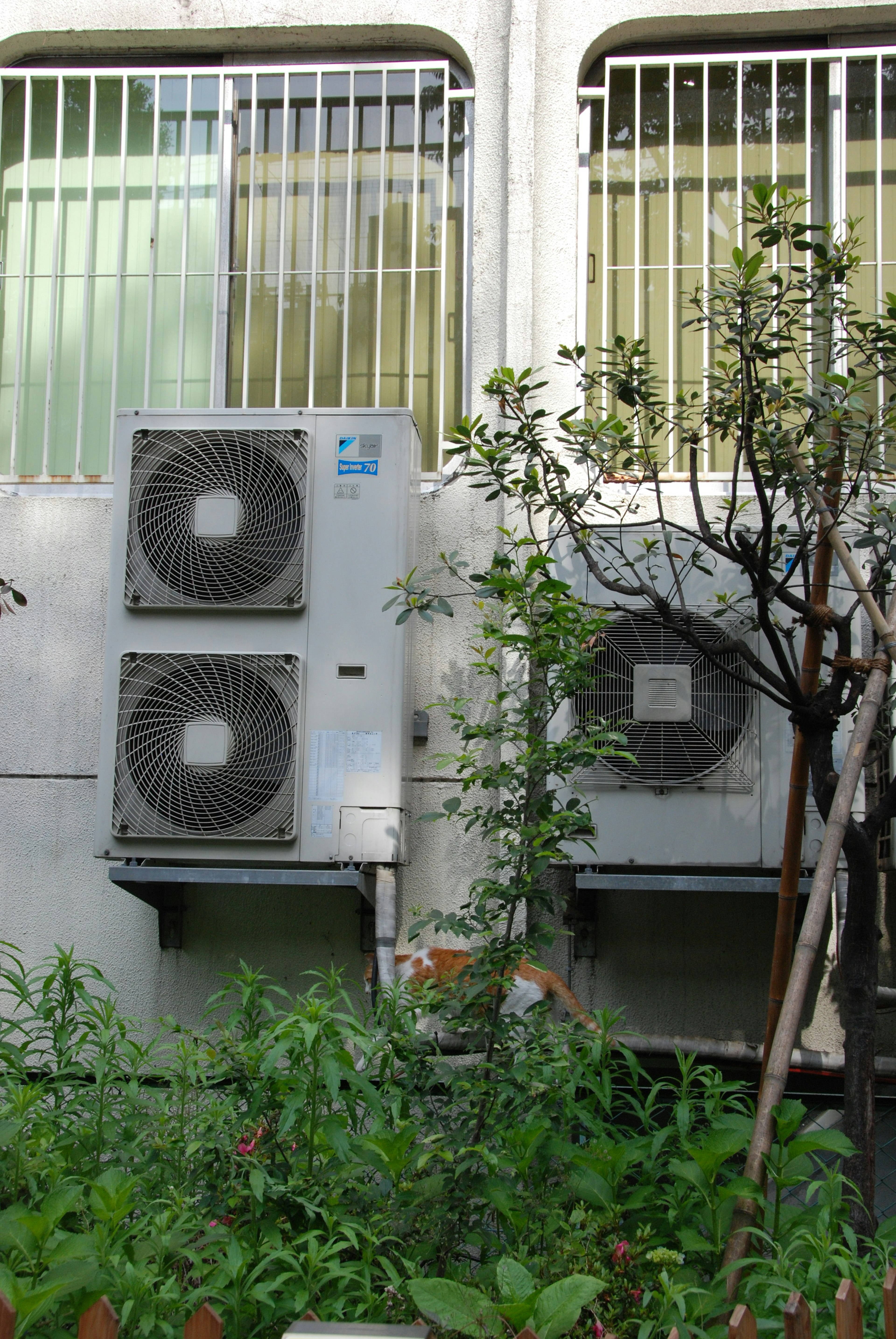 Unités de climatisation montées sur un mur de bâtiment entourées de plantes vertes