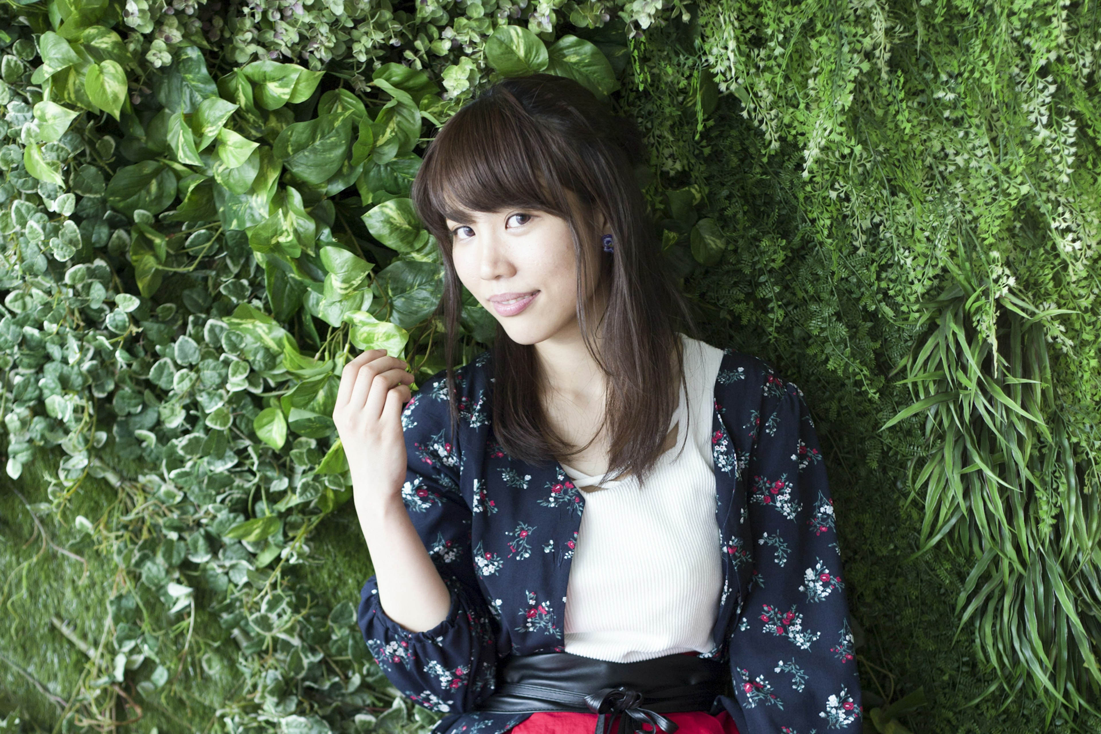 Une femme posant devant un mur de plantes vertes en souriant