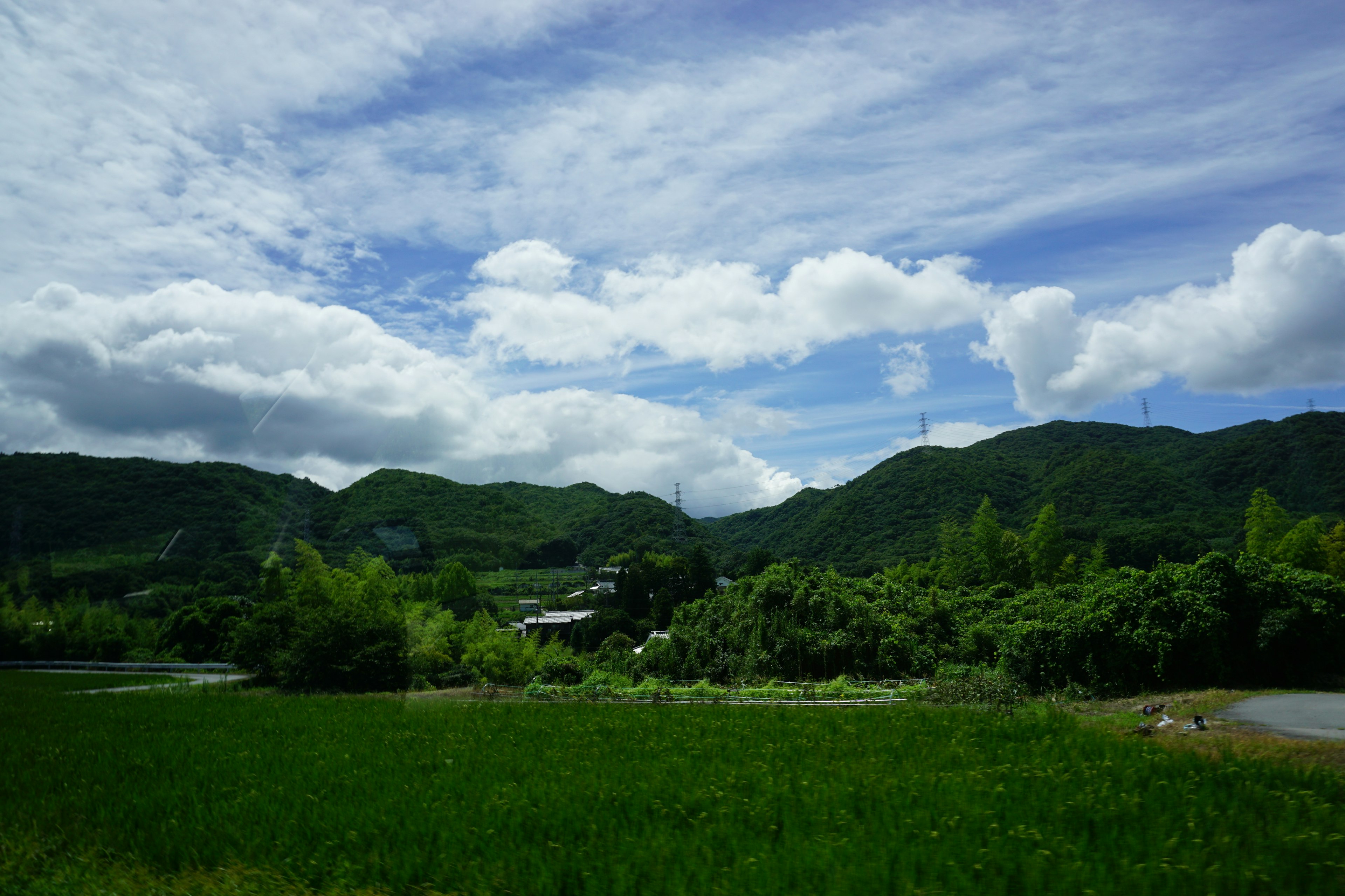 青い空と白い雲に囲まれた緑豊かな山々と田んぼの風景