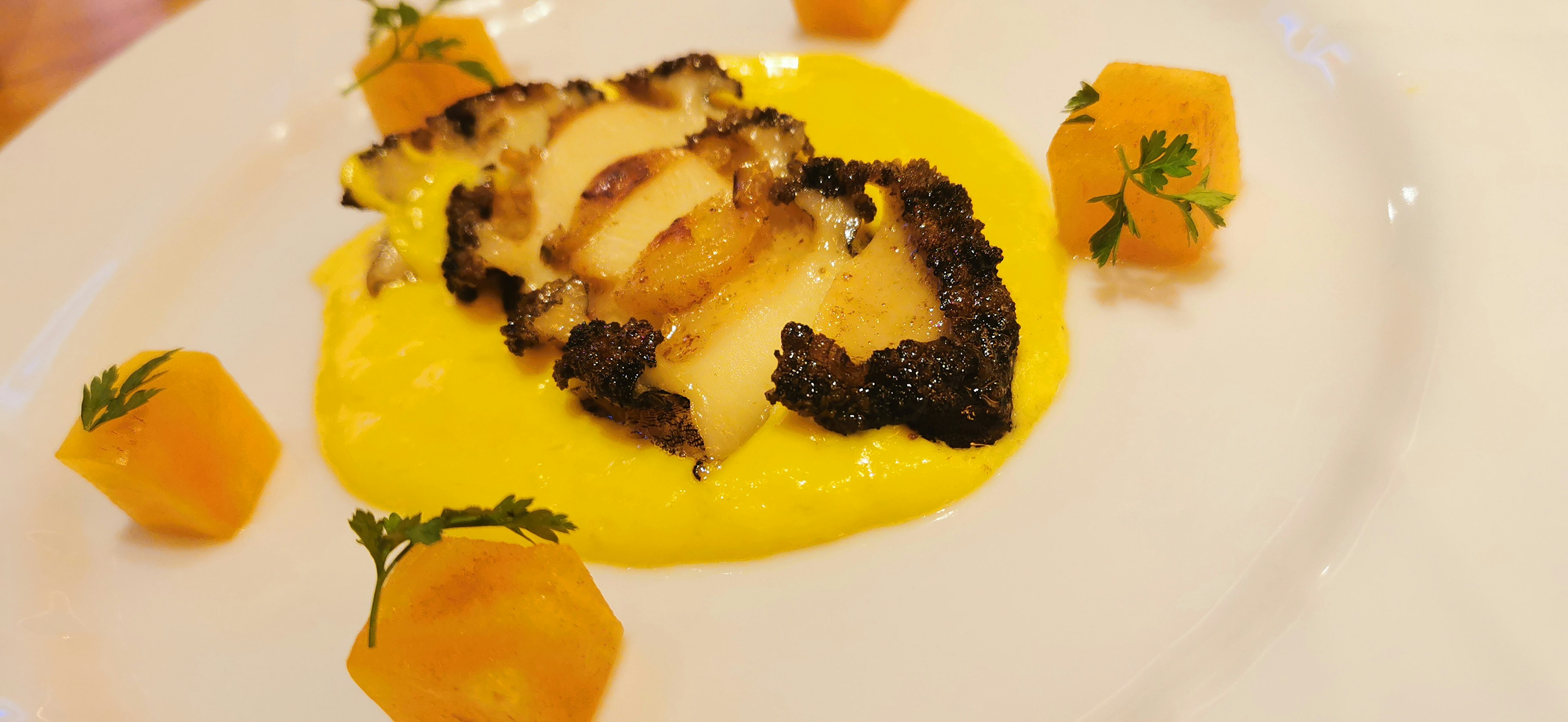 Filete de pescado a la parrilla con bordes carbonizados servido sobre una salsa cremosa con cubos de calabaza