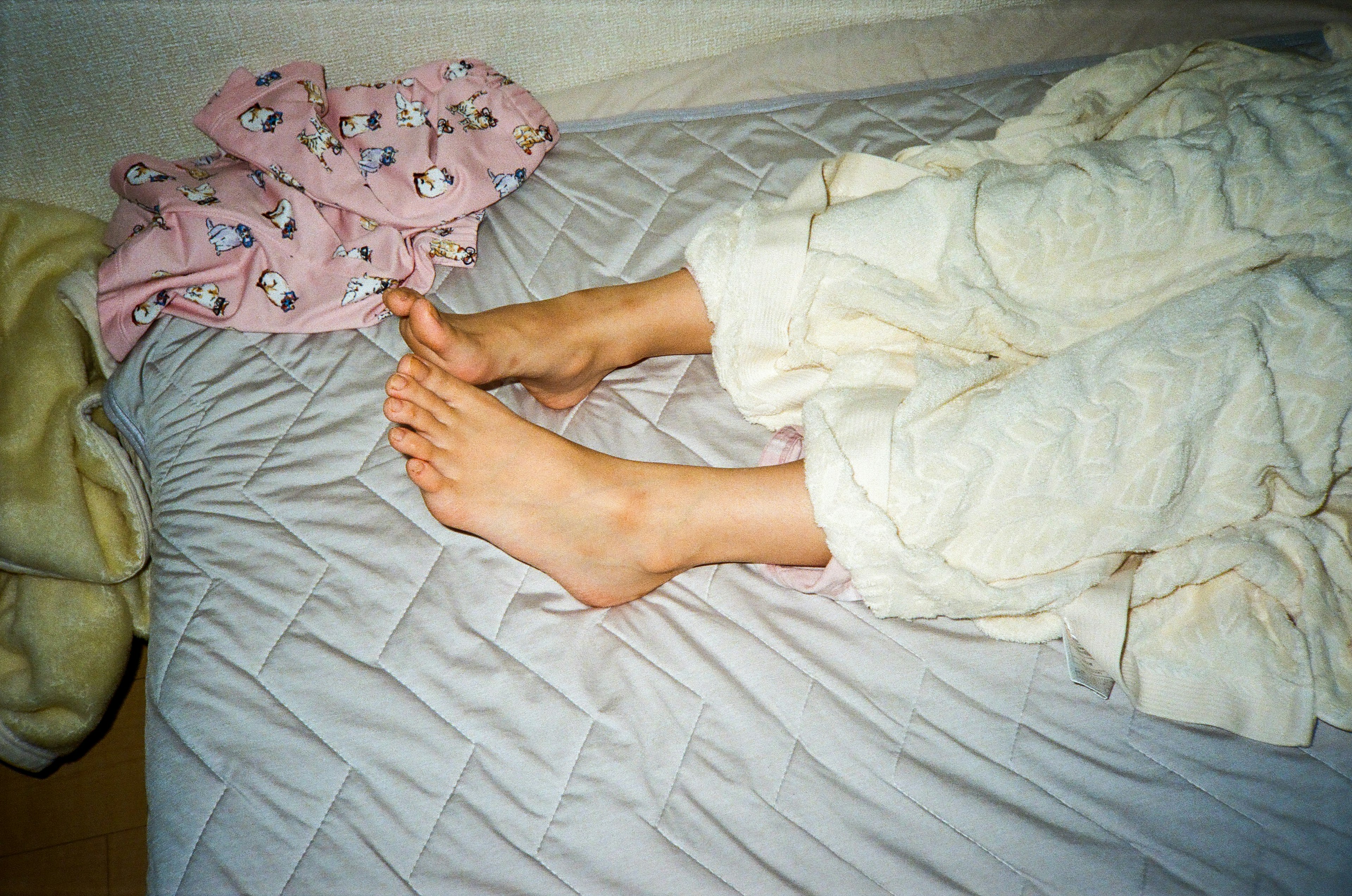 Feet visible under a white blanket on a bed with a pink blanket